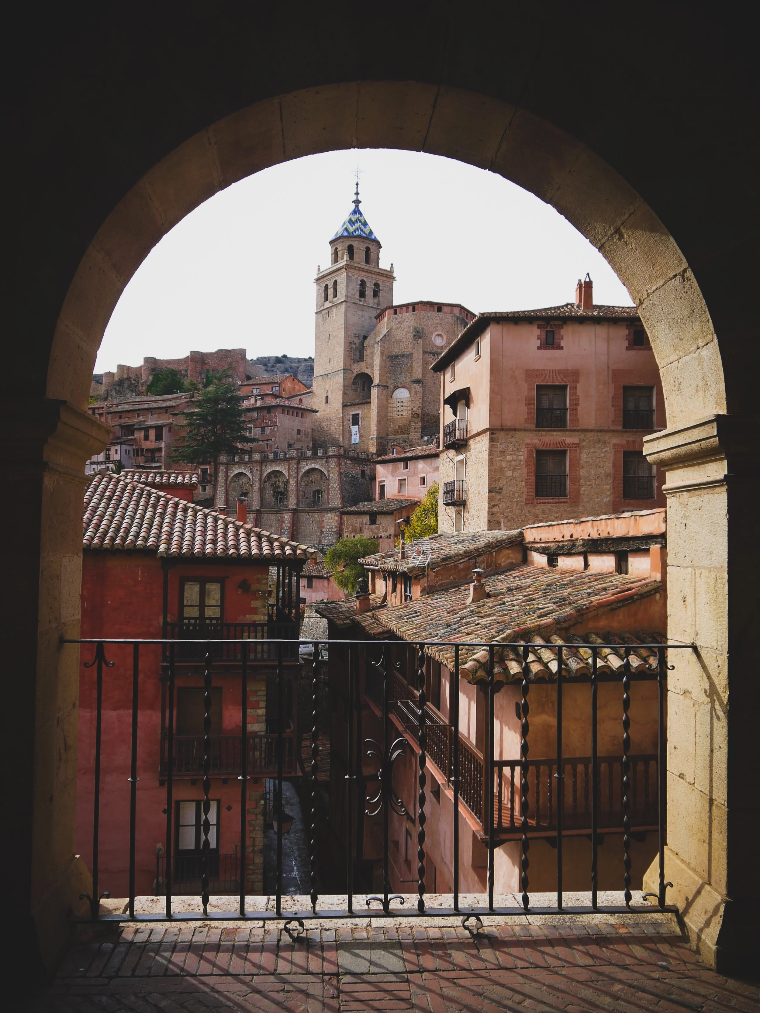 View of historic buildings and a church with a bell tower framed by an archway.