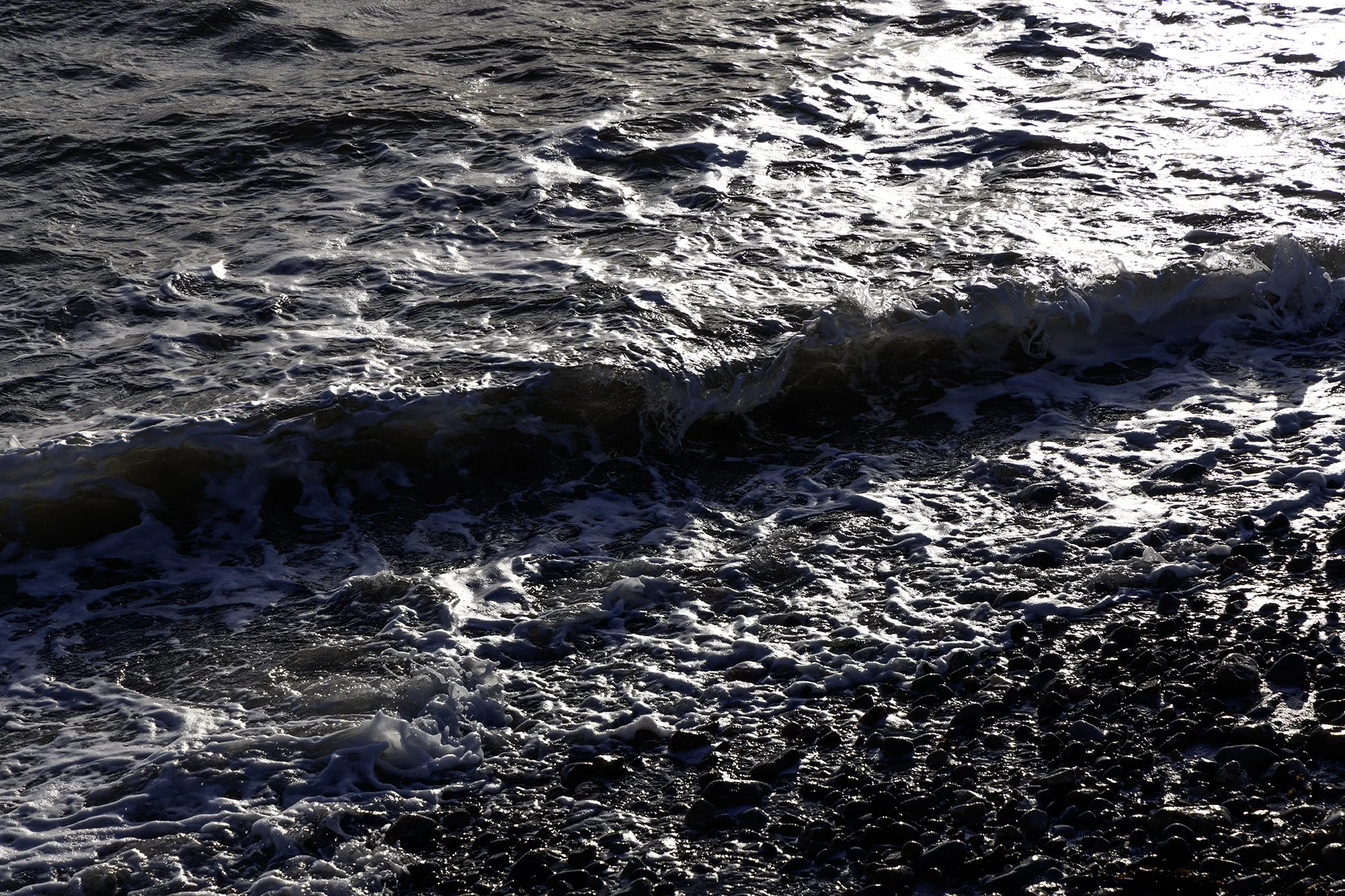 The beach in Salthill Galway watching the ocean waves hitting the shoreline with sunlight reflecting off the water.