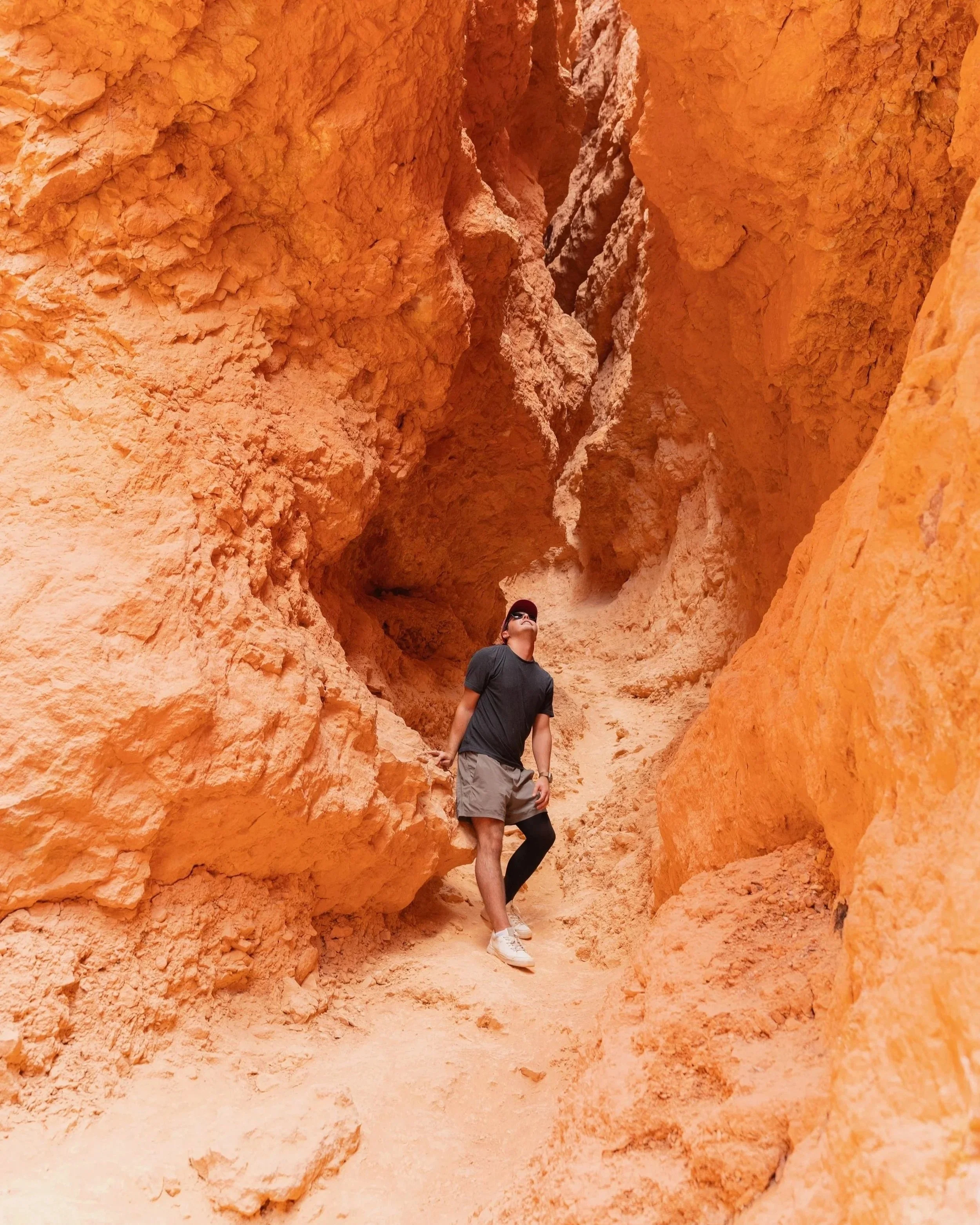 Alex Zacney standing in a narrow, orange slot canyon, looking up at the towering rock formations.