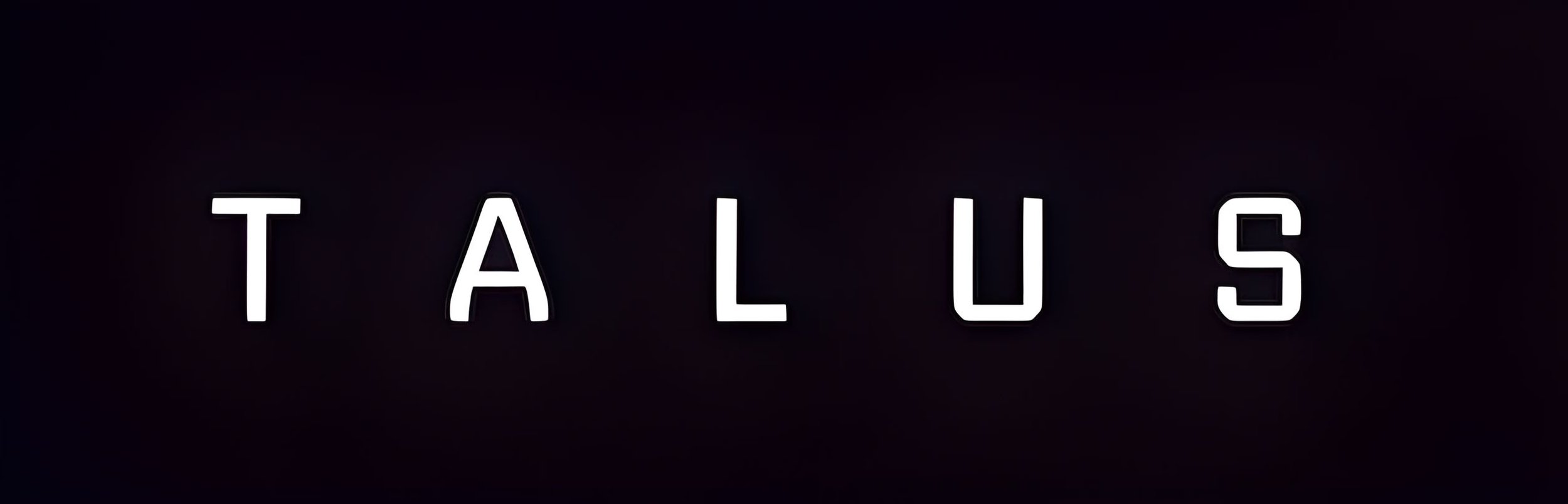 Neon sign spelling out 'TALUS' in white letters on a dark background.