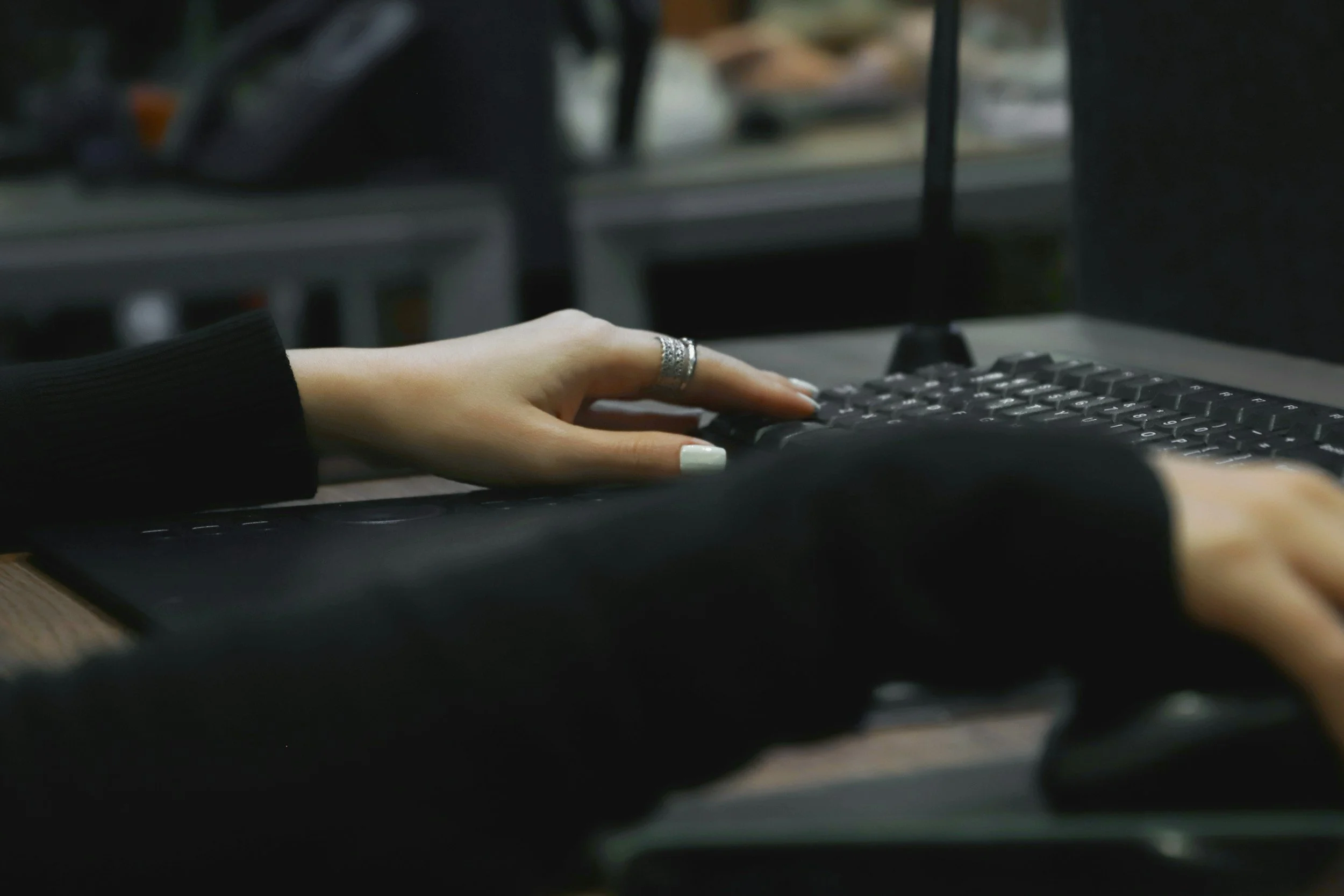 Close-up of a person's hands typing on a black computer keyboard in a dimly lit workspace.