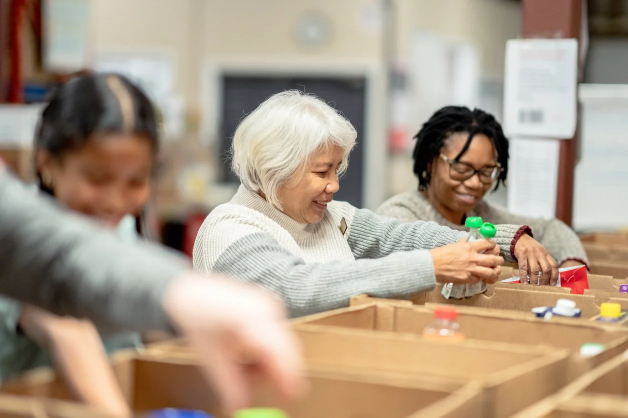 Three women smiling and organizing items in a thrift store or donation center.