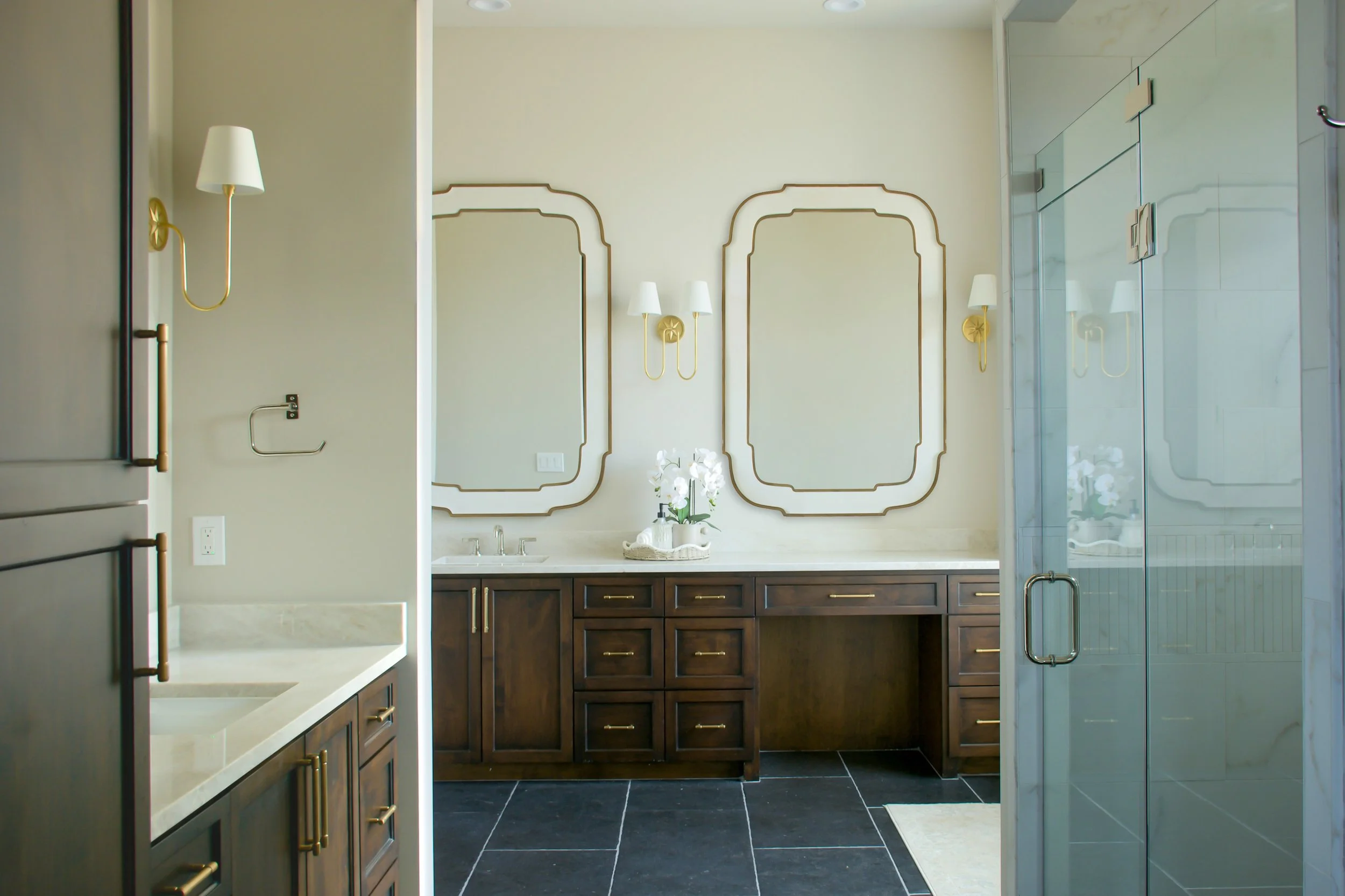 Modern bathroom with double vanity, large mirrors, white flowers, and a walk-in shower with glass door.