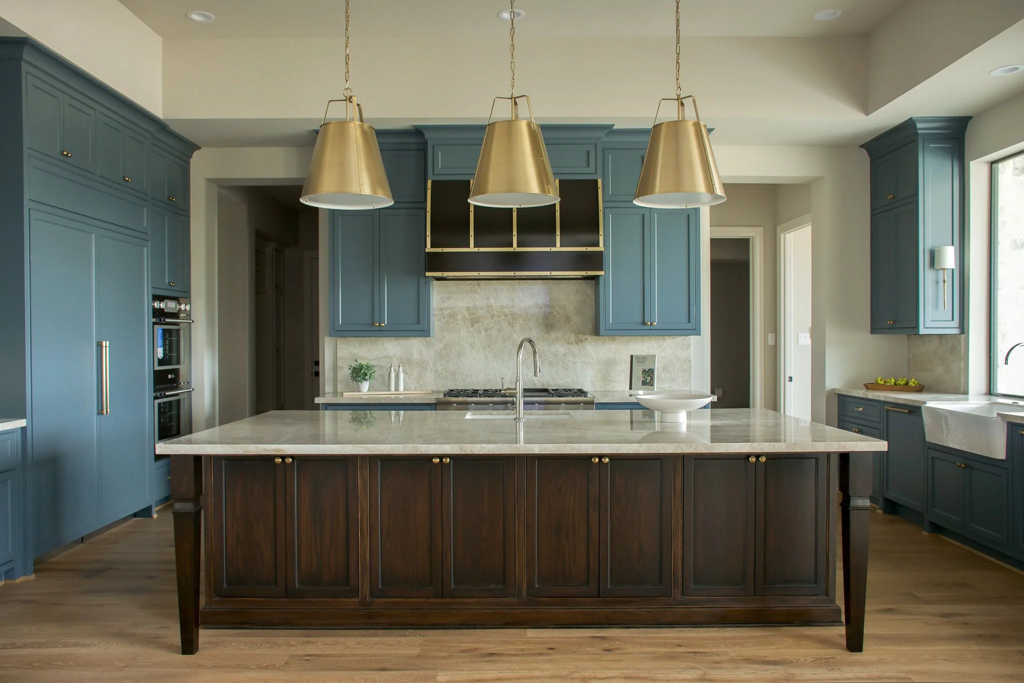 Modern kitchen with blue cabinetry, a large white marble island, gold pendant lights, and a stainless steel oven.