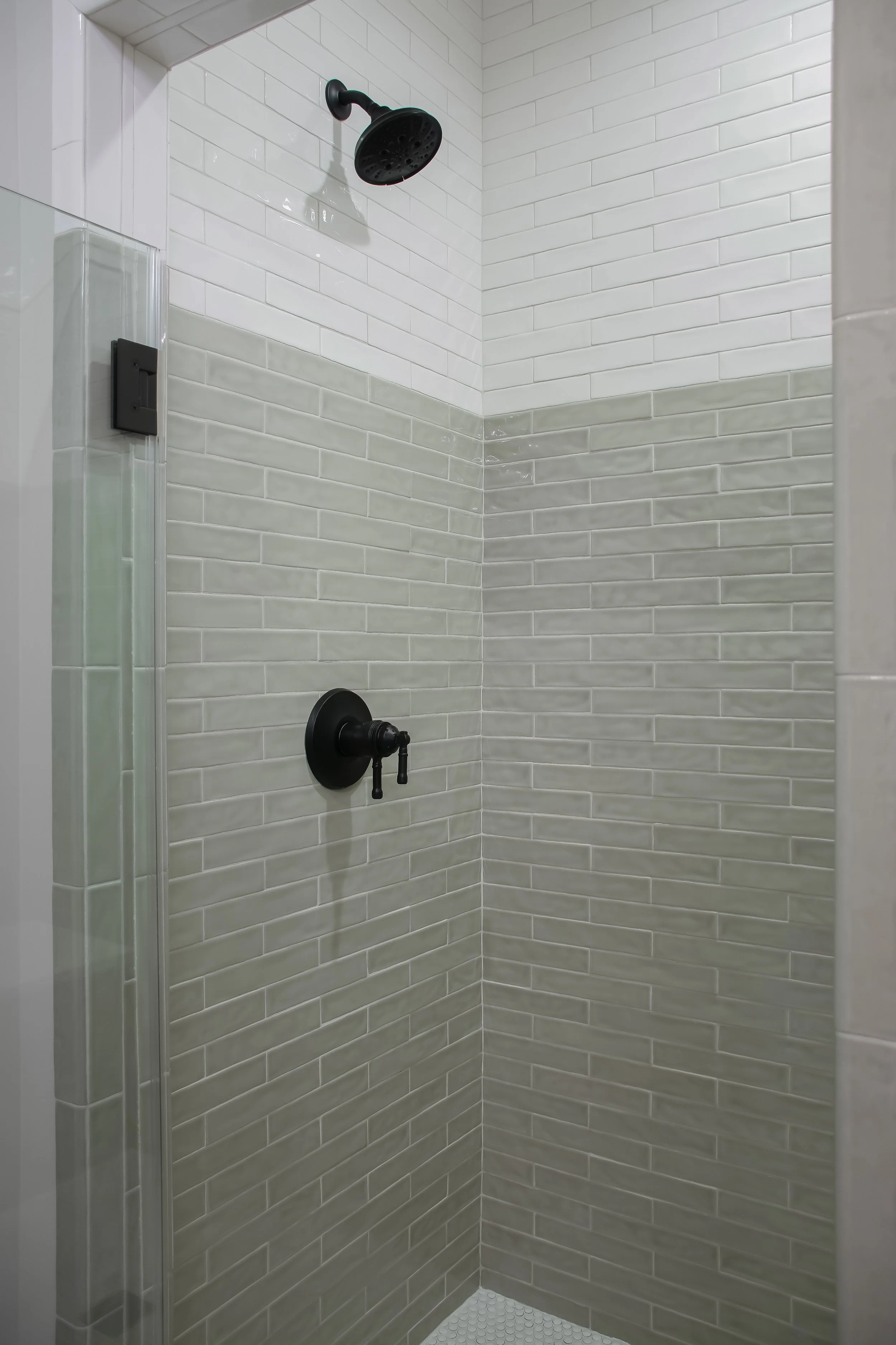 A modern shower with white subway tile on the walls and black fixtures, including a showerhead and handheld shower, with a glass door.