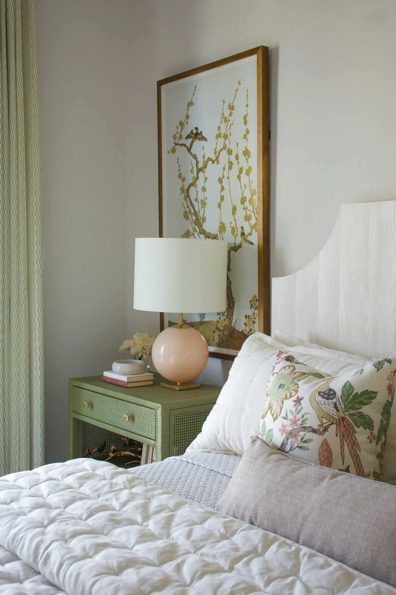 A bedroom with a bed, a green nightstand, a lamp, and floral and bird-themed art on the wall.