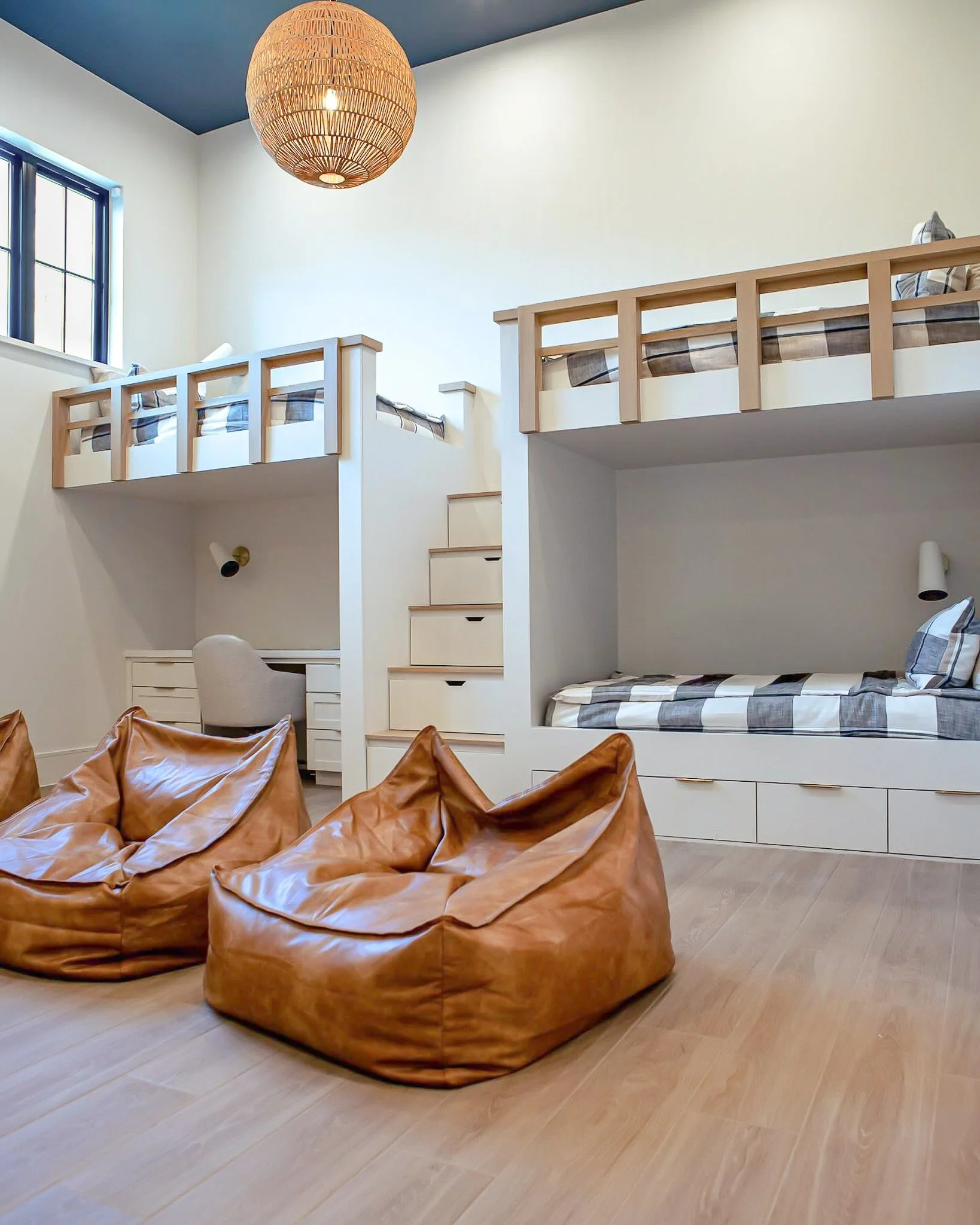 A modern loft-style bedroom with a loft bed area, a leather bean bag chair, and a desk with a chair, wooden flooring, a window, and a blue ceiling.