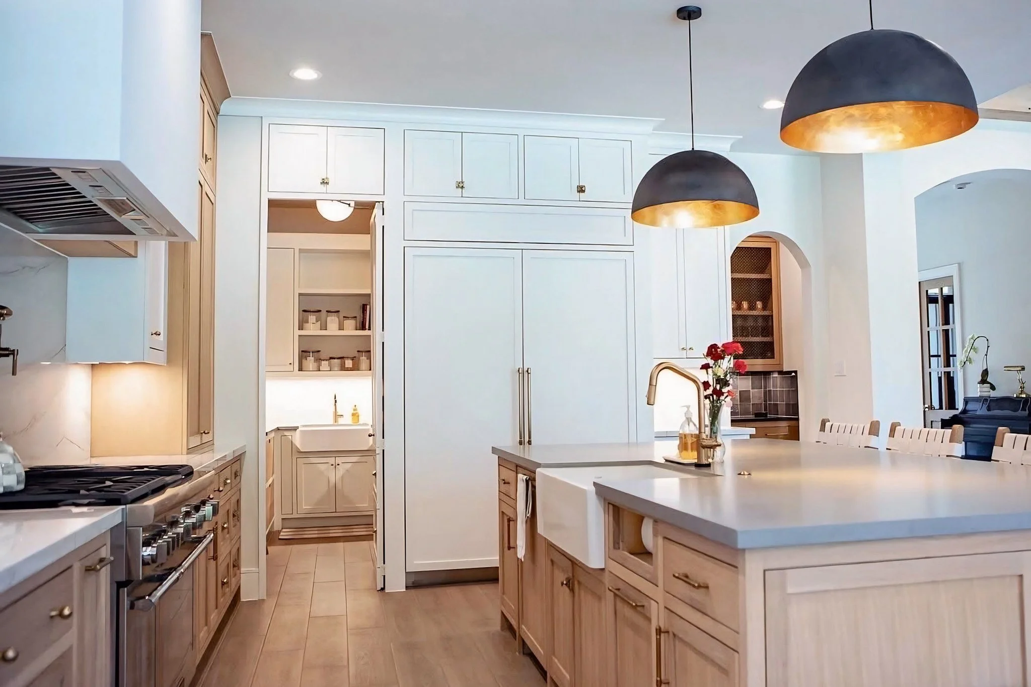 A modern kitchen with white cabinetry, wooden accents, pendant lighting, and a central island with a flower vase.