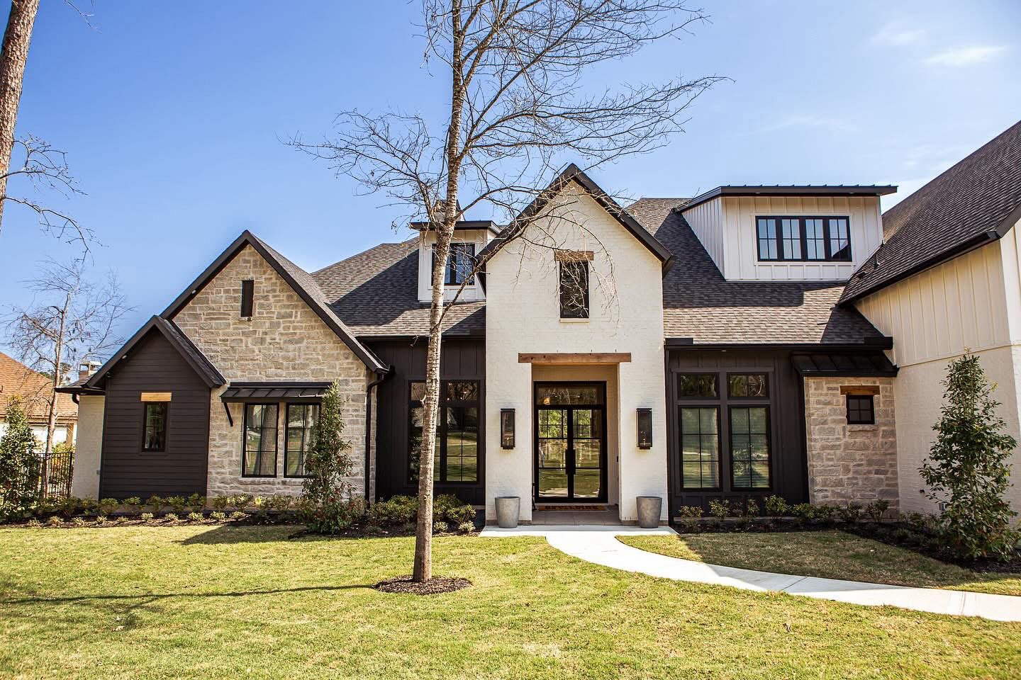 Front view of a modern, multi-story house with a landscaped lawn and trees.