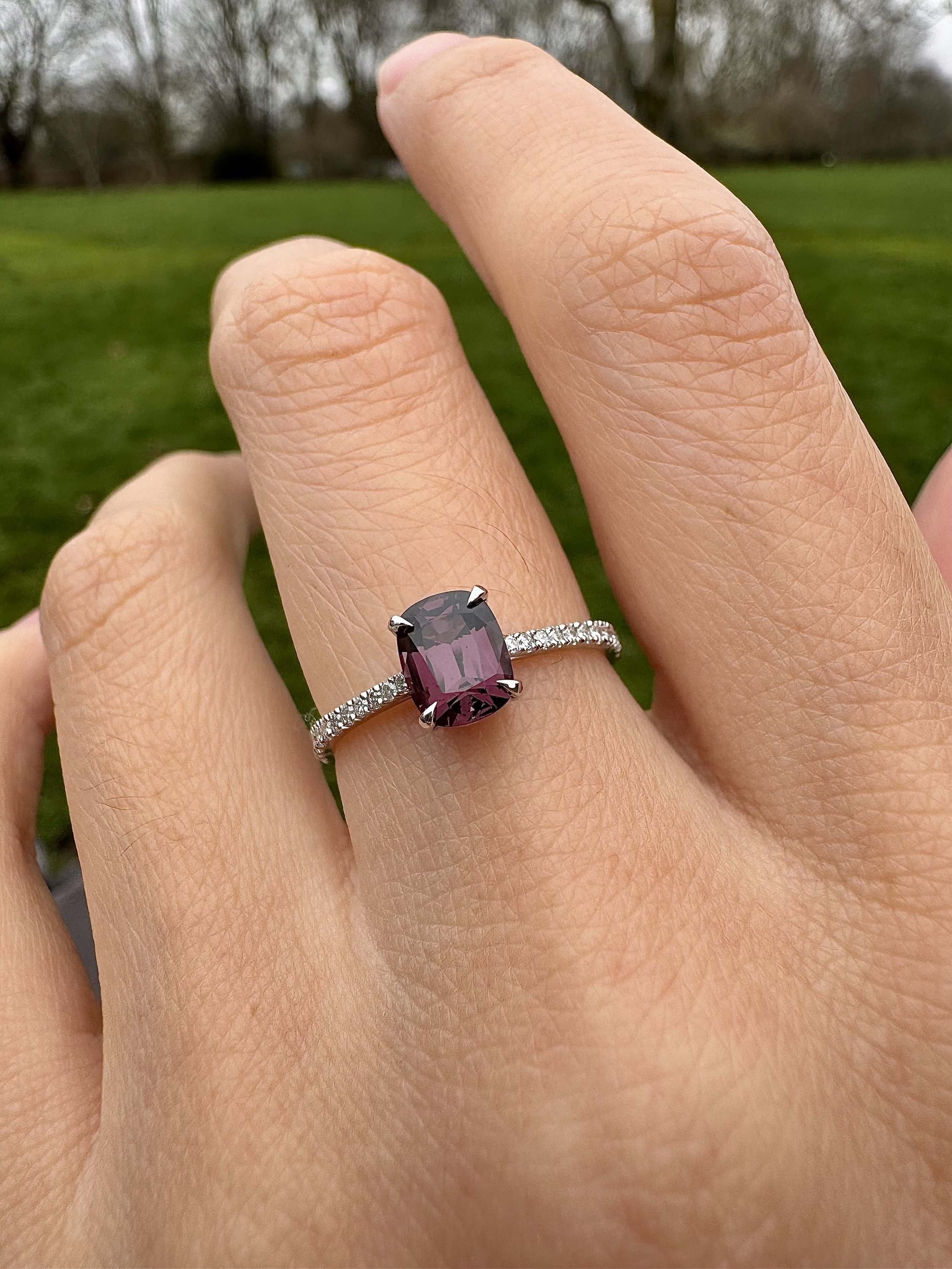 Cushion cut magenta spinel ring in white gold with hand set micro pavé diamond shoulders, worn on the hand outdoors.