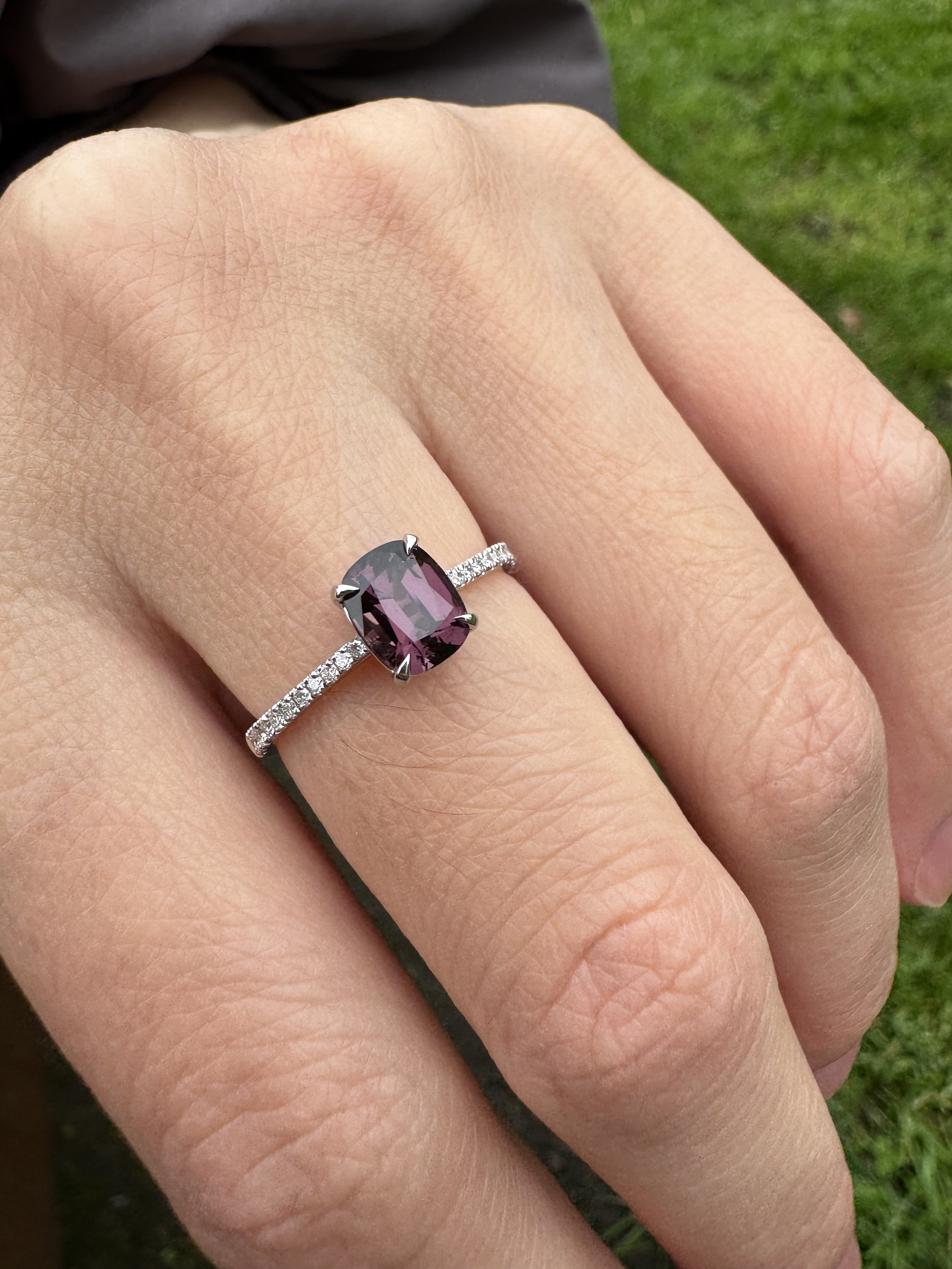 Magenta spinel solitaire in white gold with a micro pavé diamond band, worn on the hand in daylight, London made.