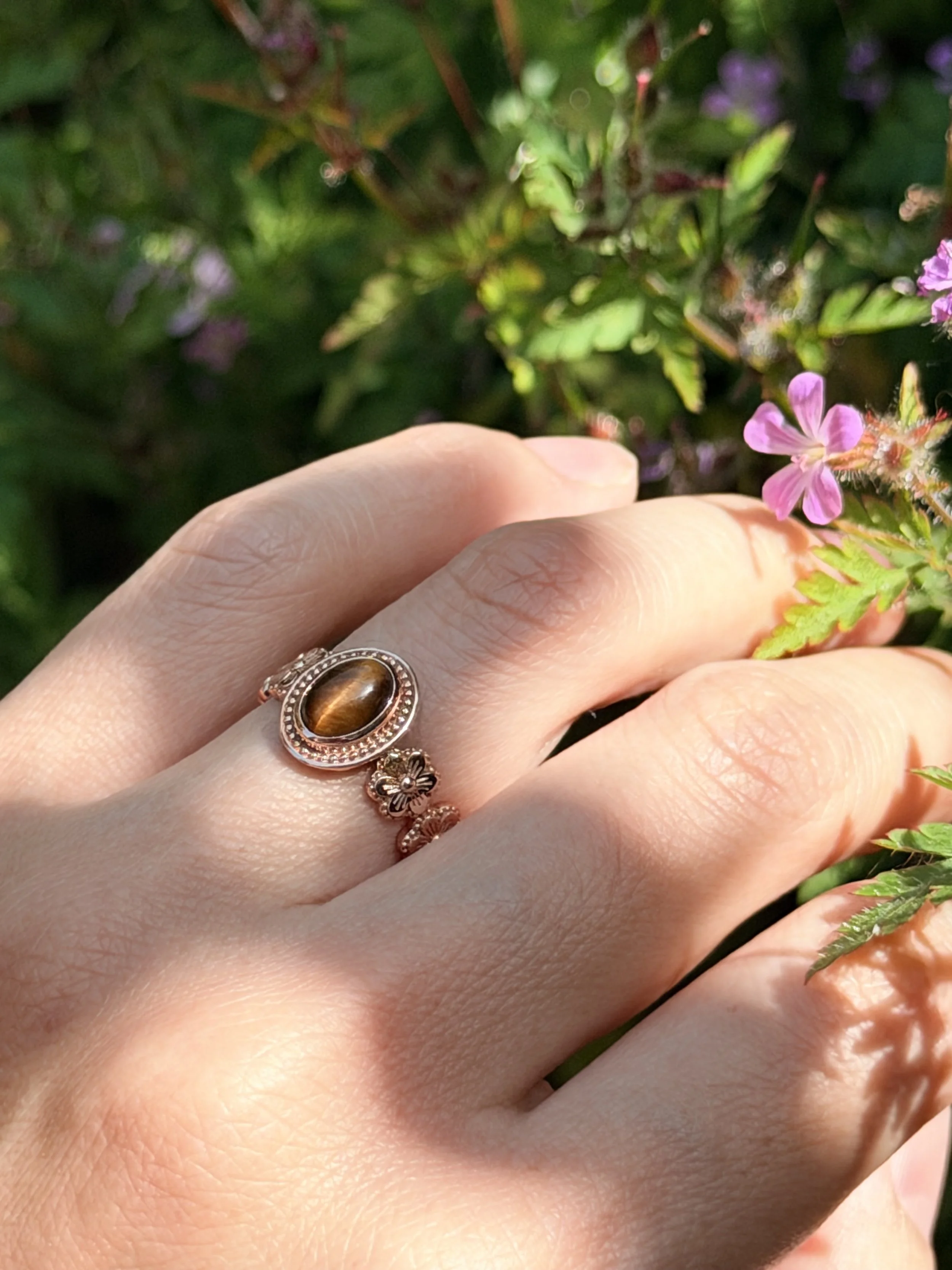 Wildflower Ring worn on hand among wildflowers — natural tiger's eye cabochon ring in 14K rose gold, handcrafted in London by Gugunava Jewelry