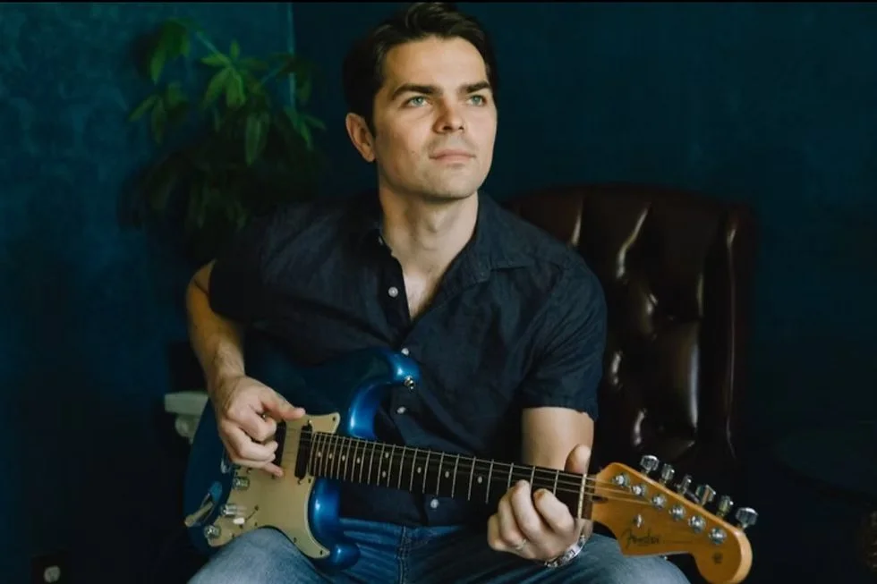 Andy Kahrs seated in a chair holding a guitar in promotional picture for show at David's 105 Listening Room on June 13.
