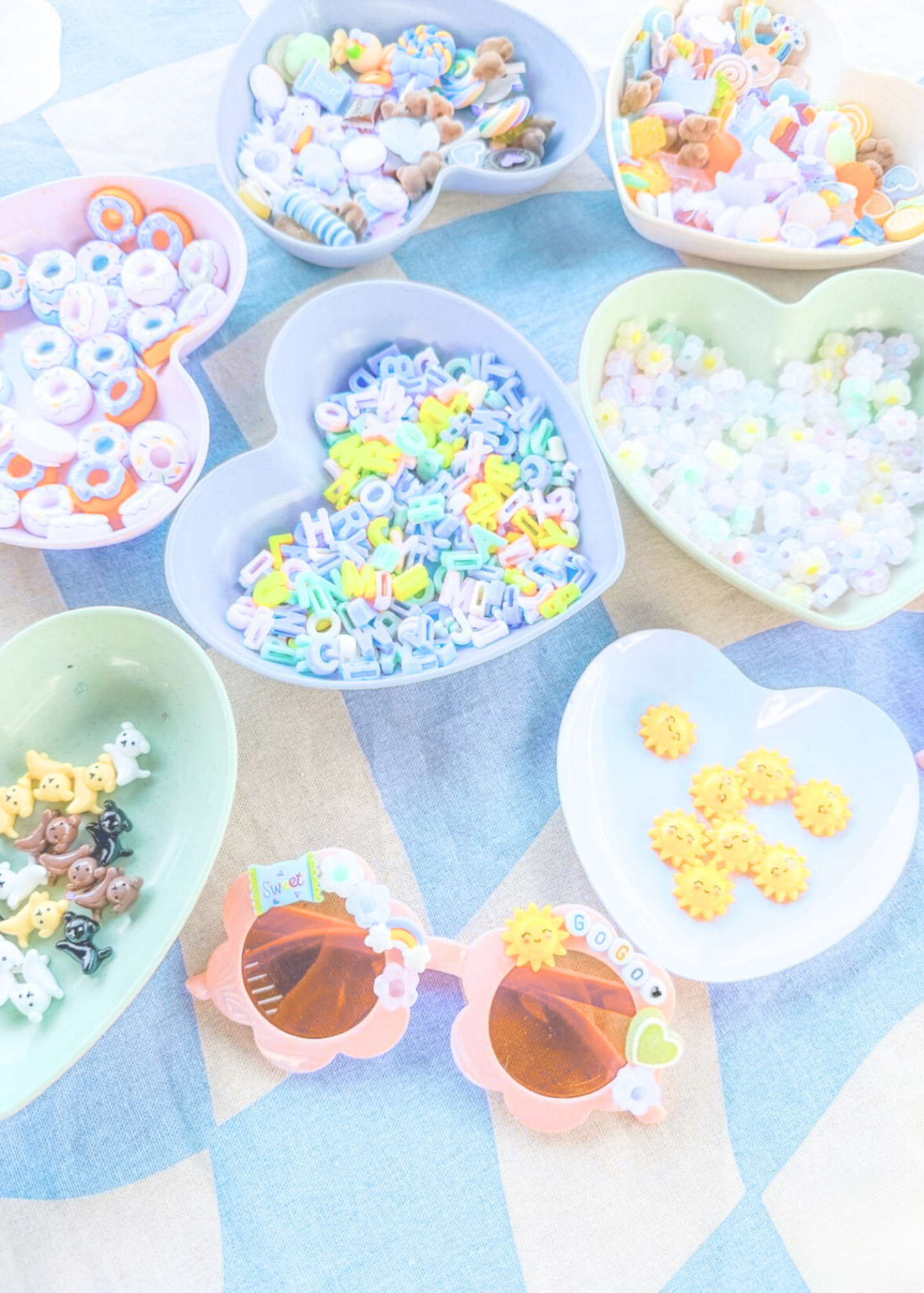 Colorful candy and snack bowls shaped like hearts, with various candies including gummy bears, sprinkles, and decorative sugar shapes, on a pastel-colored table.