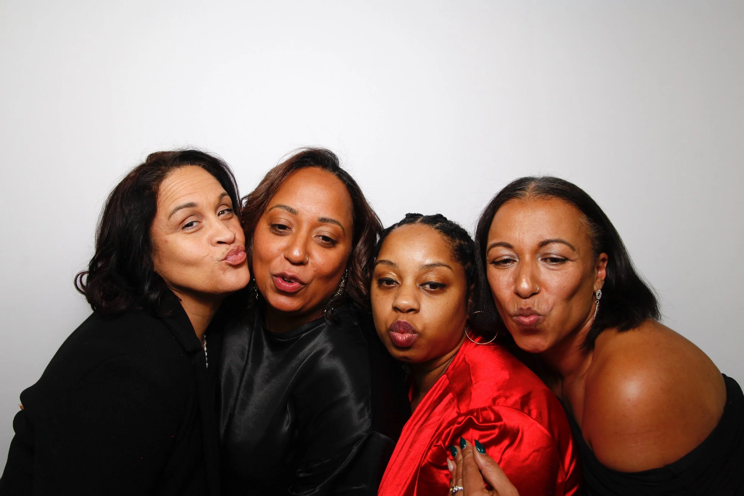 Four women in a close group, making kissy faces at the camera against a plain white background.