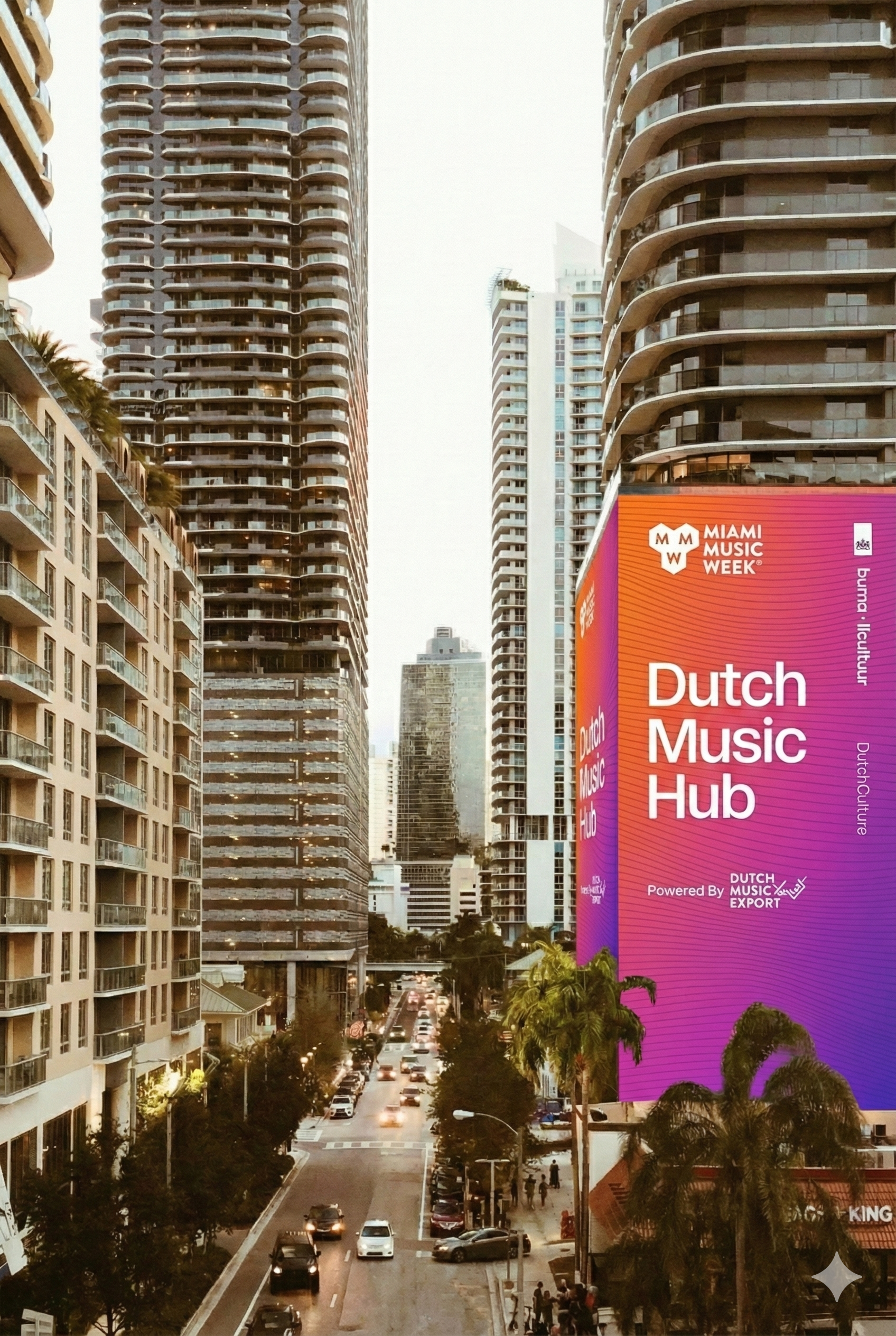 Cityscape of Miami with tall buildings and a large digital billboard advertising Dutch Music Hub during evening hours. Cars are on the street, and palm trees are visible in the foreground.