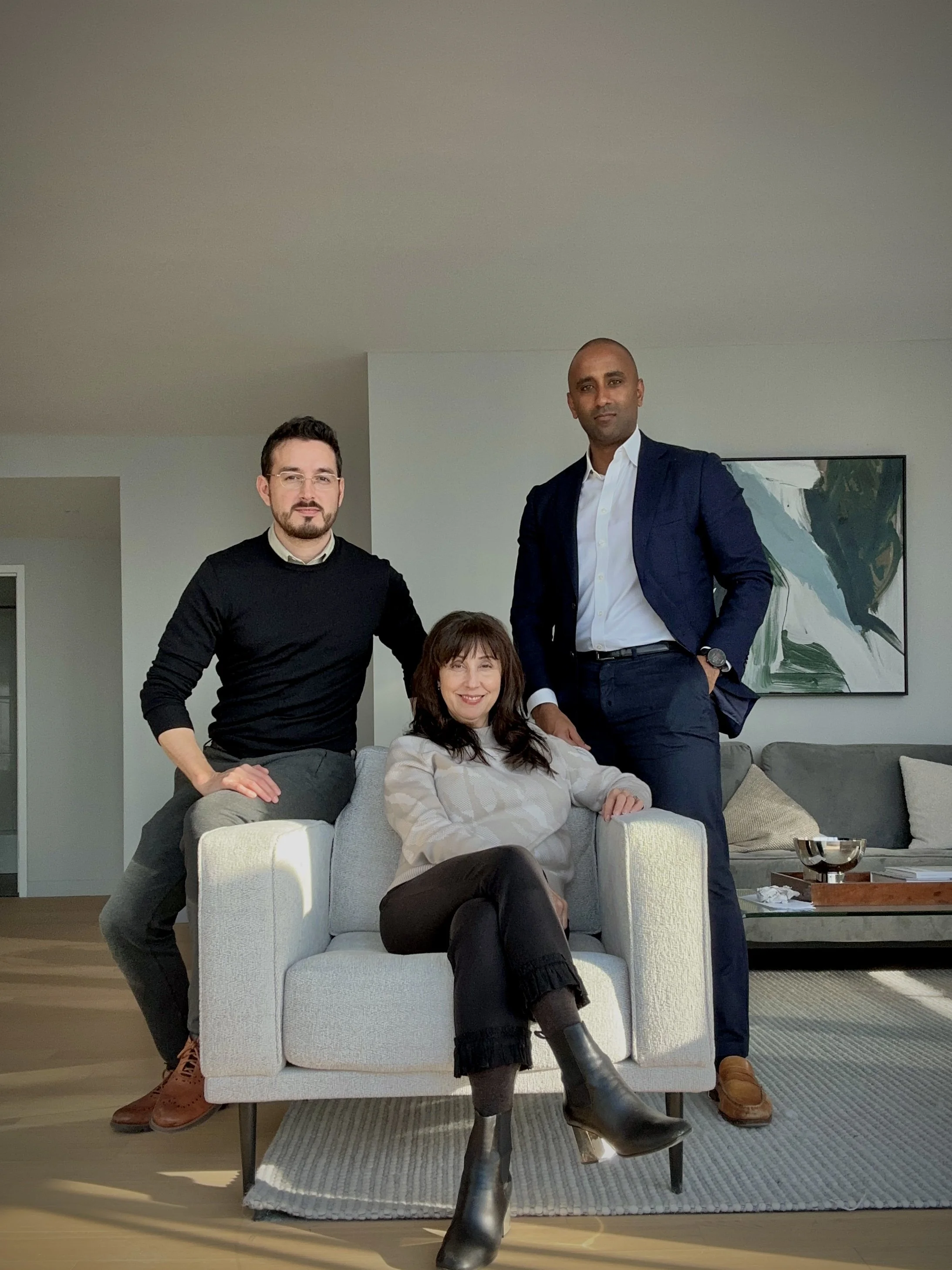 Three people posing in a modern living room, two men and one woman, with a light-colored couch, side table, and artwork.