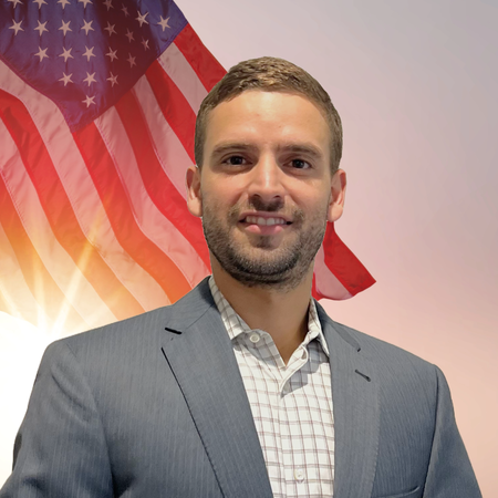 A man in a suit standing in front of an American flag.