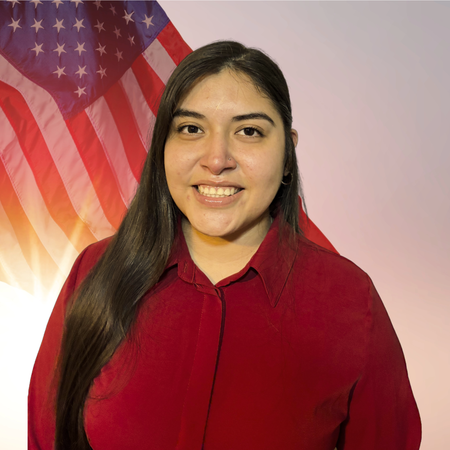 A young woman with long dark hair smiling, wearing a red shirt, standing in front of an American flag backdrop.