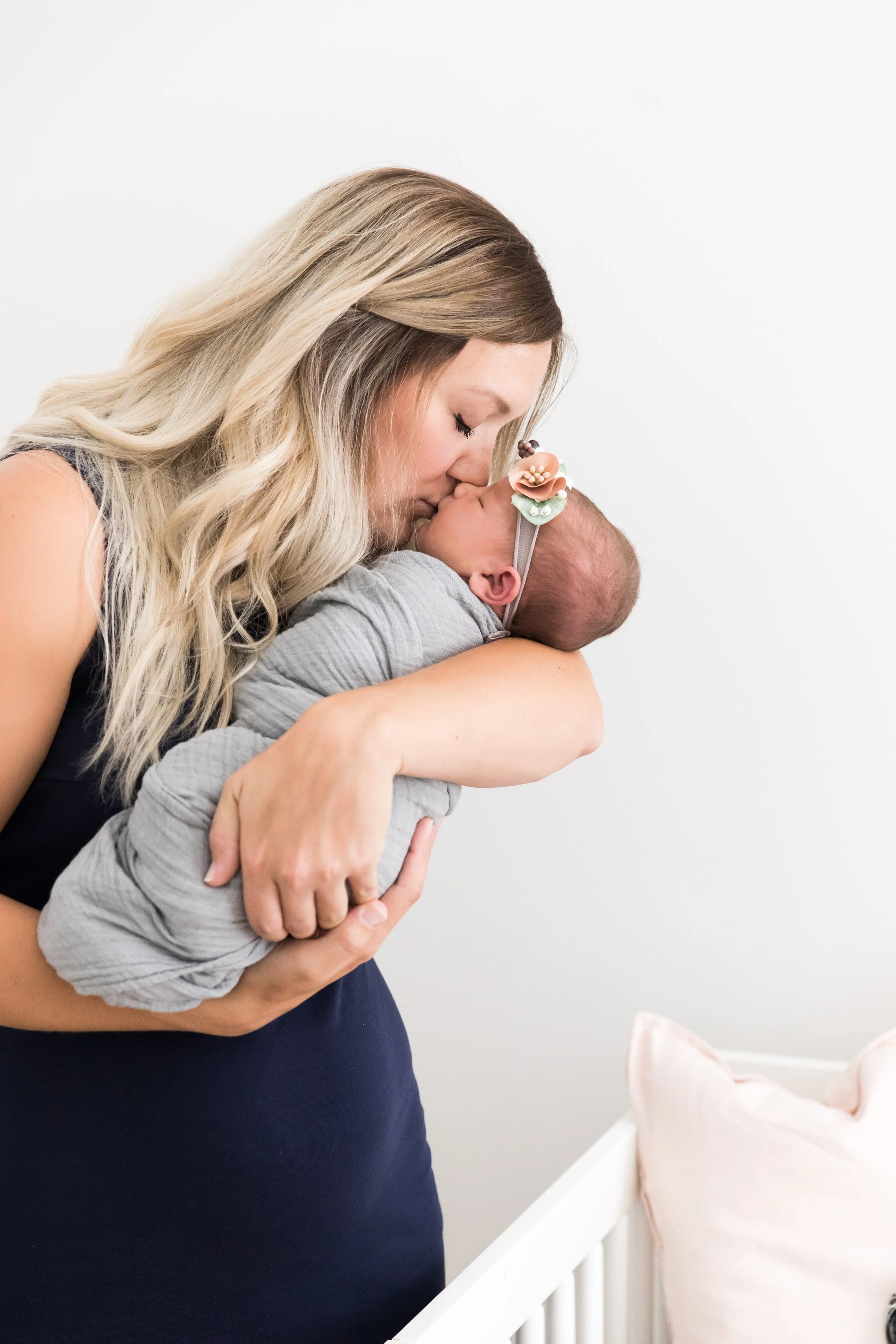 A mother holding her newborn baby close and kissing its forehead in a nursery setting.