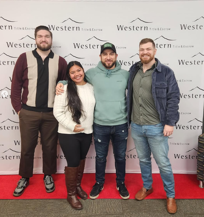 Group of four smiling people standing in front of a 'Western Title & Escrow' backdrop, with a red carpet under their feet.