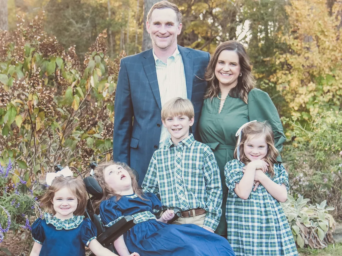A family of six posing outdoors in a garden with autumn leaves, smiling at the camera.