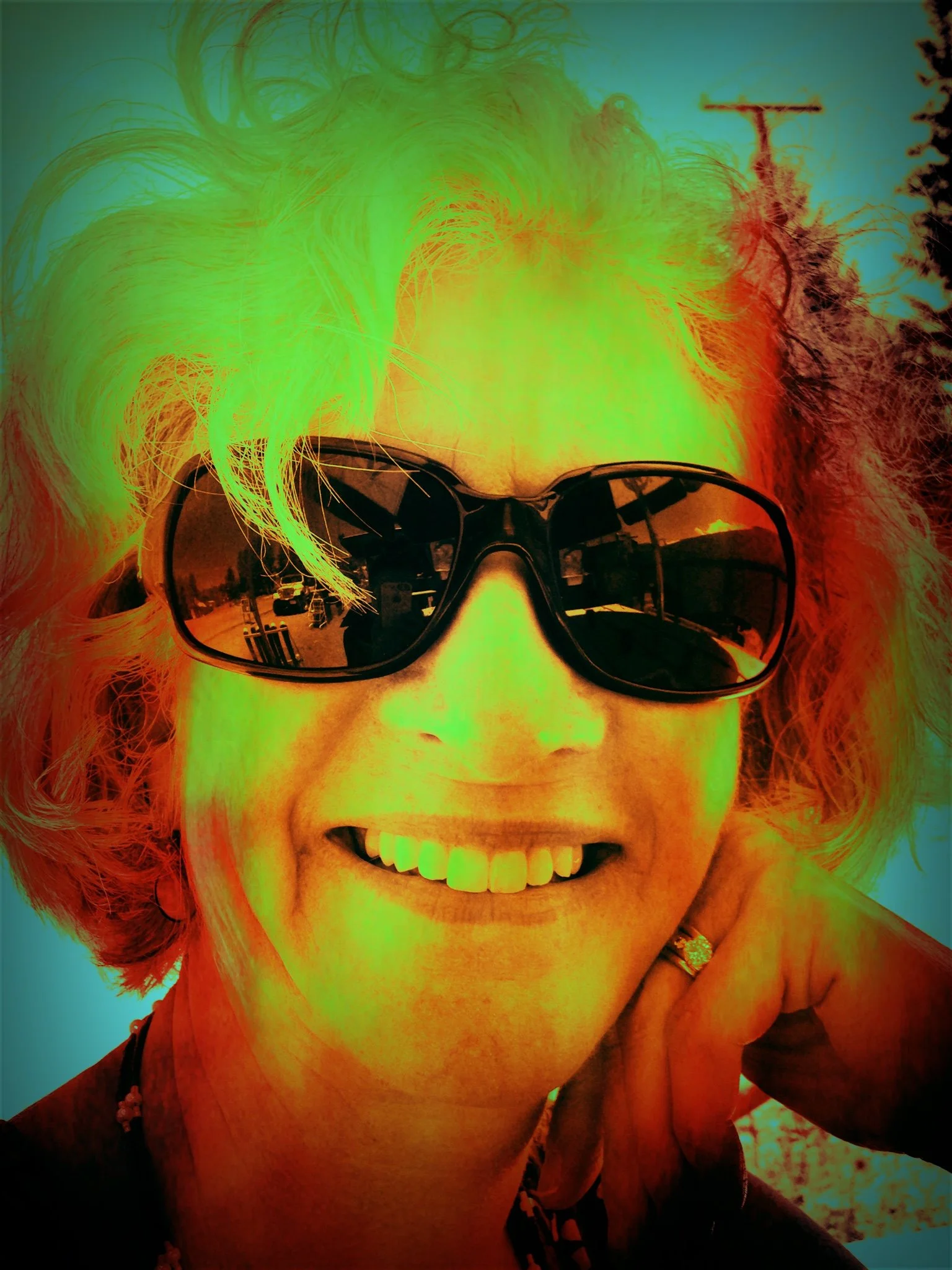 Person with curly hair and wearing sunglasses smiling.