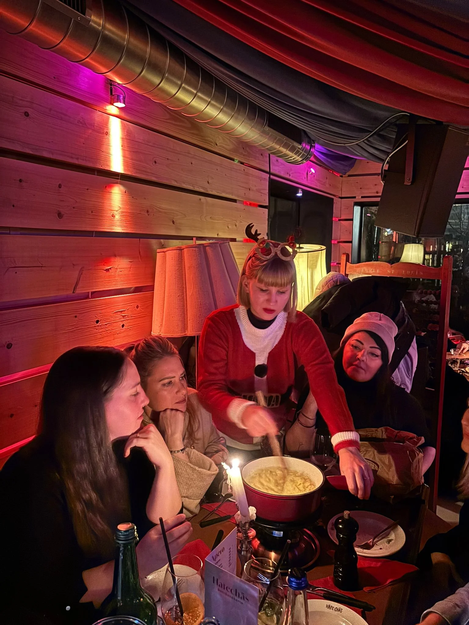 Menschen sitzen um einen Tisch in einem festlich dekorierten Restaurant, während eine Frau in einem Weihnachtskostüm Suppe serviert.