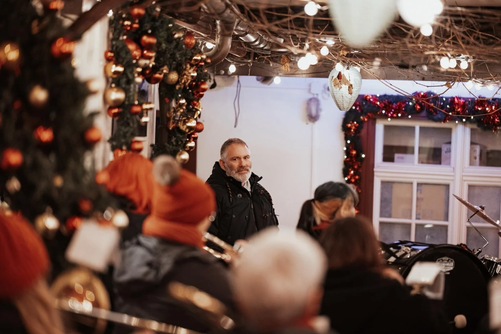 Festlich geschmückte Weihnachtsfeier mit Musik, Weihnachtsbaum und Weihnachtsdeko, Menschen sitzen zusammen, einer schaut in die Kamera.