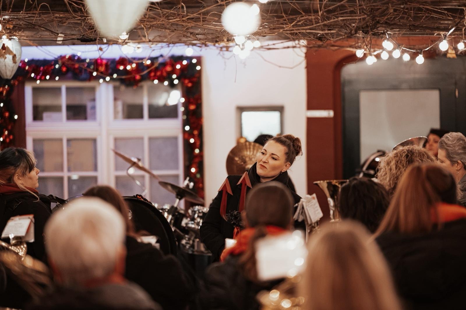Eine Gruppe von Menschen, die in einem festlich dekorierten Raum sitzen, mit einer Frau in der Mitte, die offenbar in einer Band spielt, während sie mit anderen Musikern umgeben ist.