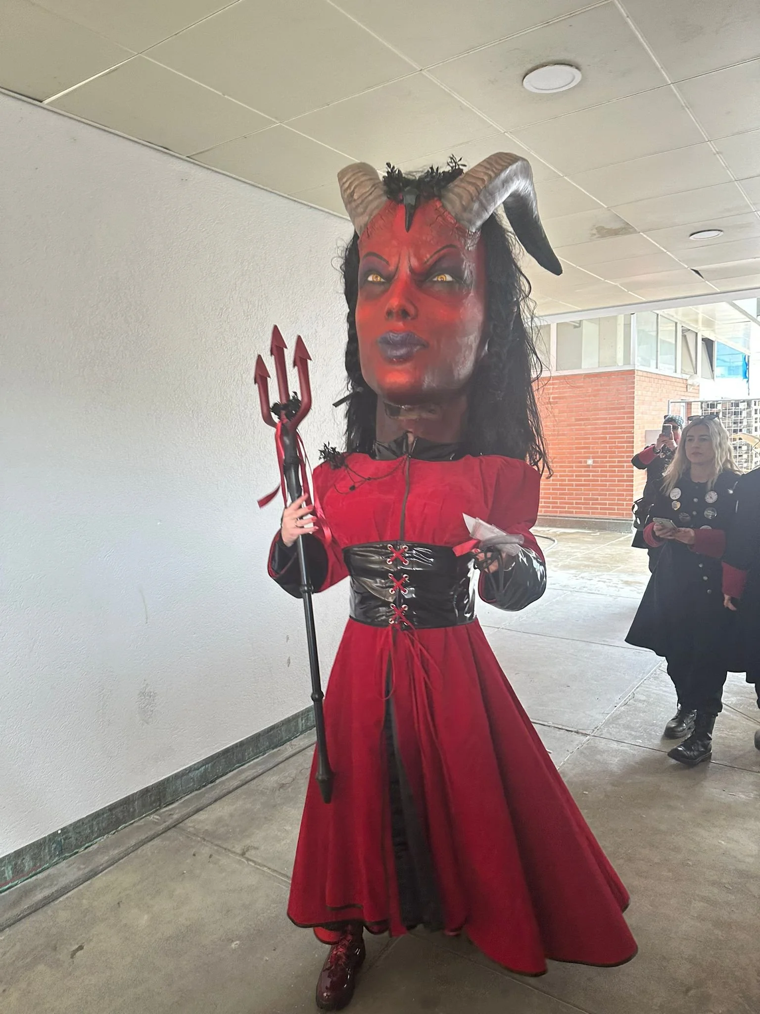 Person in Teufelskostüm mit großer Teufelsmaske, roten Kleid und Dreizack, Kostüm für Karneval oder Halloween.