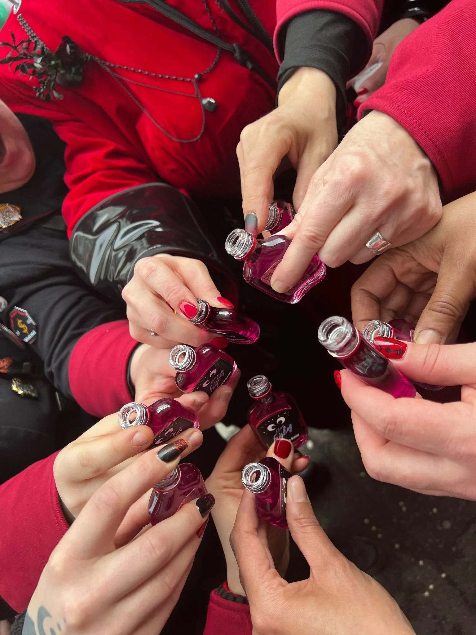 Mehrere Hände, die kleine Flaschen mit rotem Nagellack halten, im Kreis zusammengeschoben.