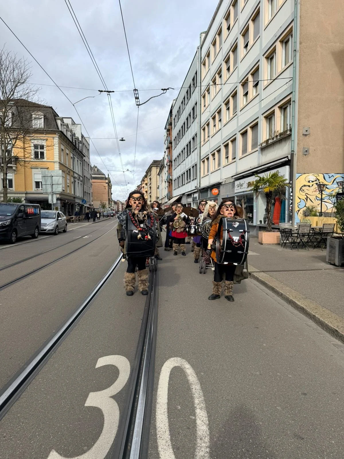 Eine Gruppe von Menschen in einer Stadt tragen Karnevalskostüme mit Tiermasken und Trommeln, die auf der Straße gehen.