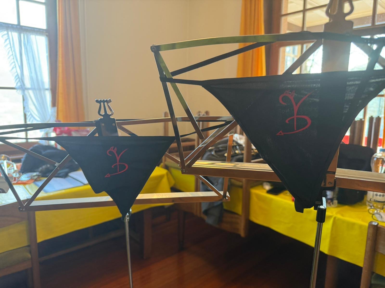 Zwei Modellschiffe mit schwarzen Segeln, die jeweils ein rotes Symbol mit der Buchstabe 'B' tragen, stehen in einem Raum mit großen Fenstern und gelben Tischtüchern.