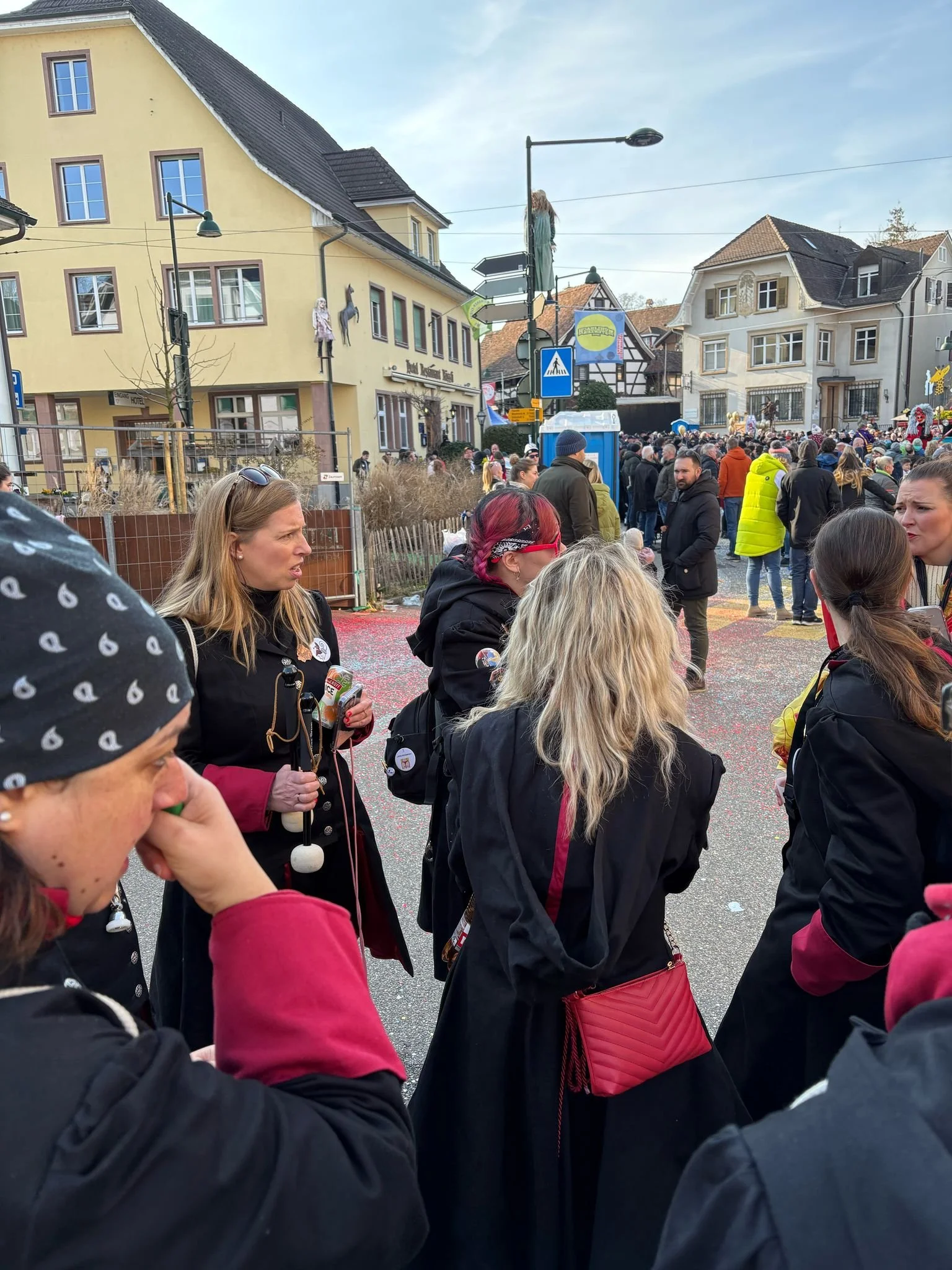 Menschen versammeln sich bei einer Veranstaltung auf einer Straße in einer Stadt mit alten Gebäuden. Es scheint ein Fest oder eine Parade zu sein.