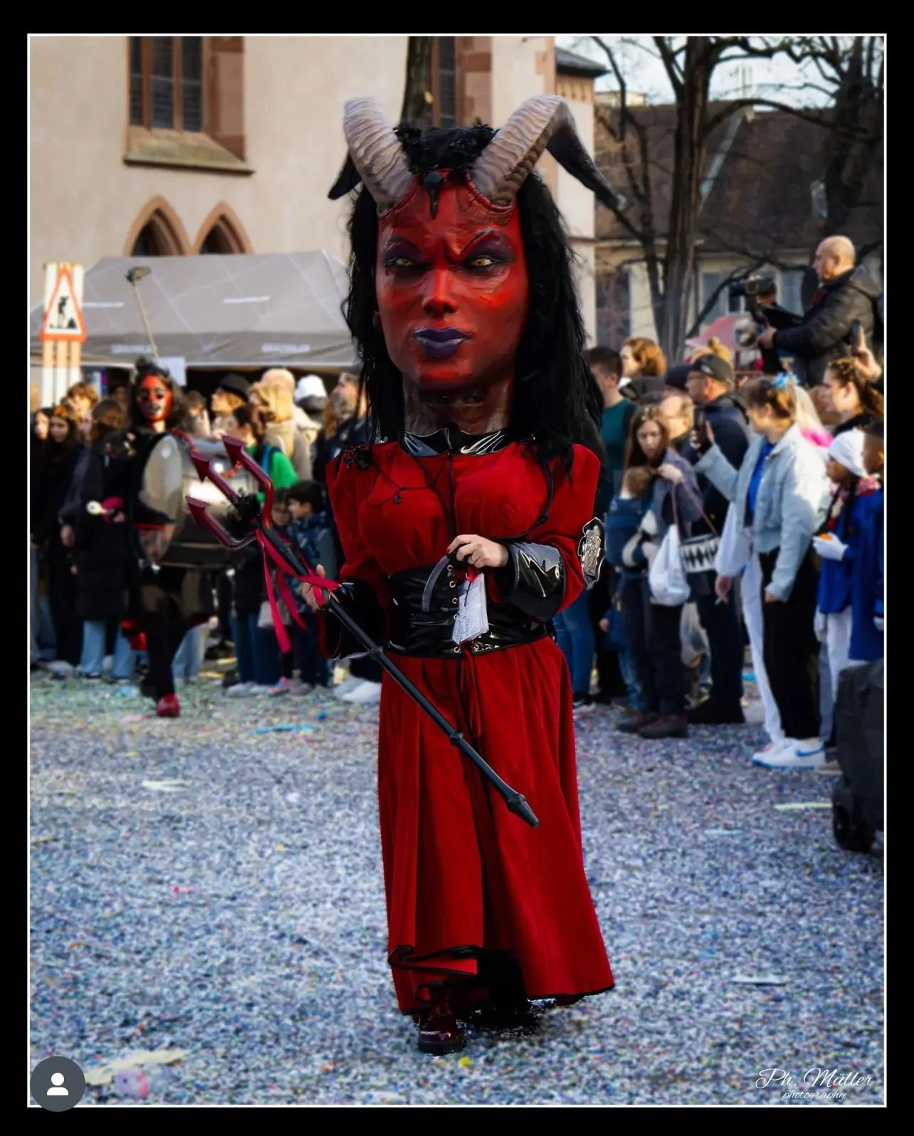 Person in Teufelskostüm mit roten Kleidern, großen Hörnern und Teufelsmaske bei einer Parade.