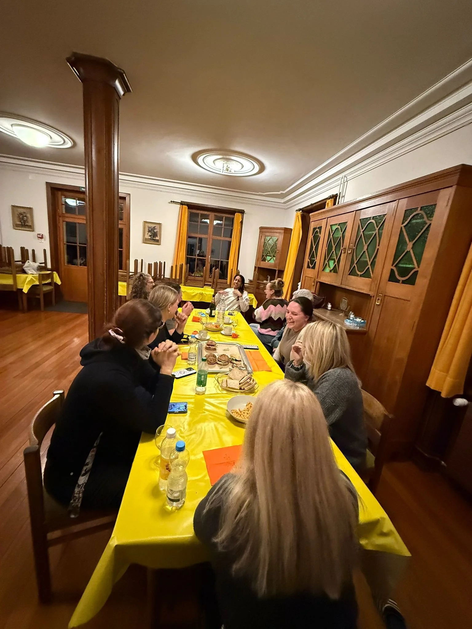 Eine Gruppe von Menschen sitzt an einem langen Tisch in einem festlich dekorierten Raum und unterhält sich beim Essen.