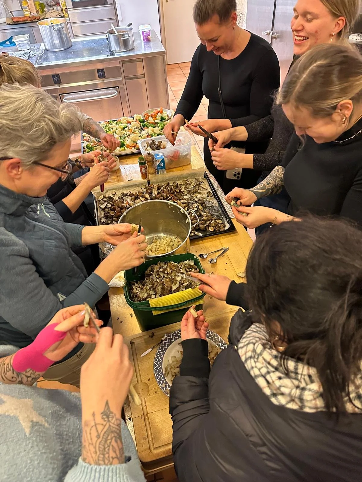 Mehrere Menschen in einer Küche, die Austern und Muscheln auf einem Tisch zubereiten und essen.