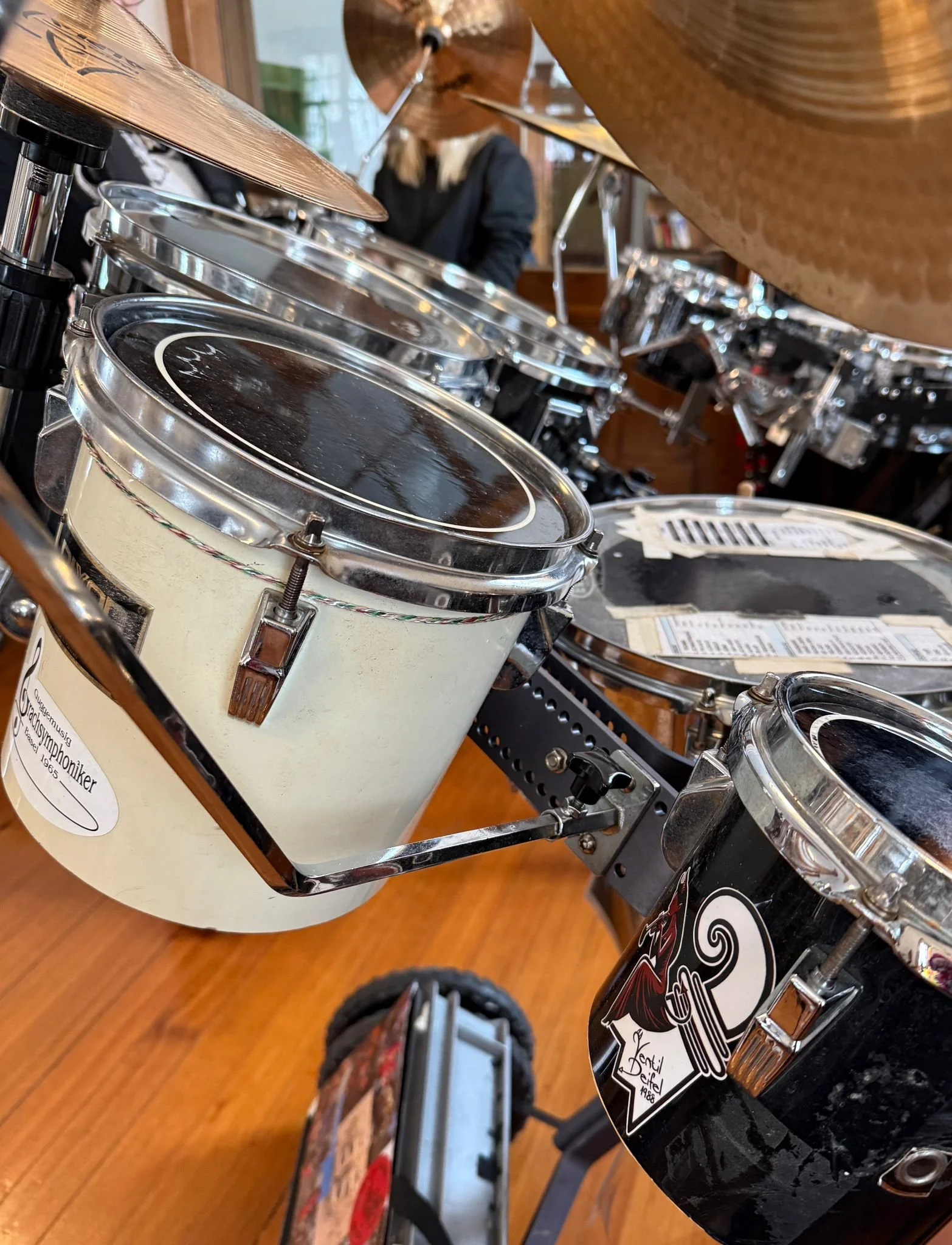 Verschiedene Musikinstrumente, darunter Snare-Drum, Tom-Toms, Becken und ein Tambourine, in einer Musikschule oder einem Proberaum.