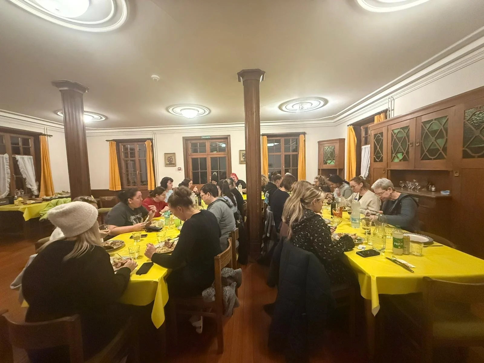 Menschen sitzen an zwei langen Tischen in einem festlich dekorierten Raum beim Essen.