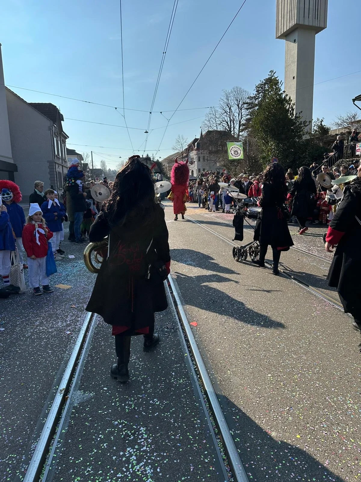 Straßenparade mit Menschen in Kostümen, Confetti, Balkon, trüger Himmel