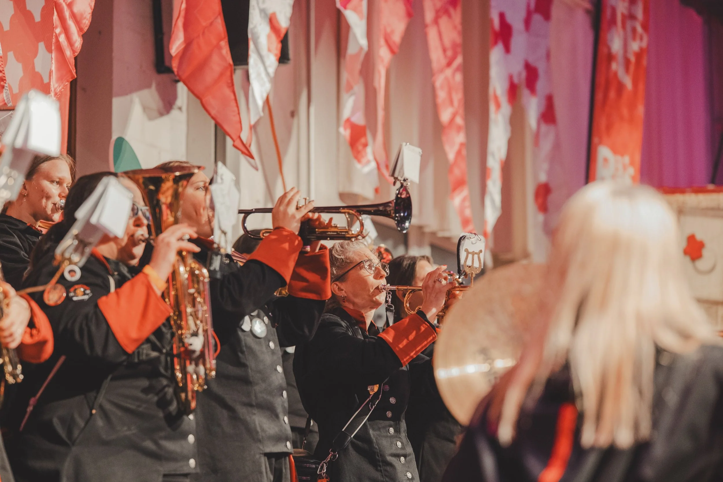 Eine Gruppe von Musikerinnen, die in einem Orchester spielen, alle tragen schwarze Uniformen mit roten Akzenten, während sie auf der Bühne auftreten.