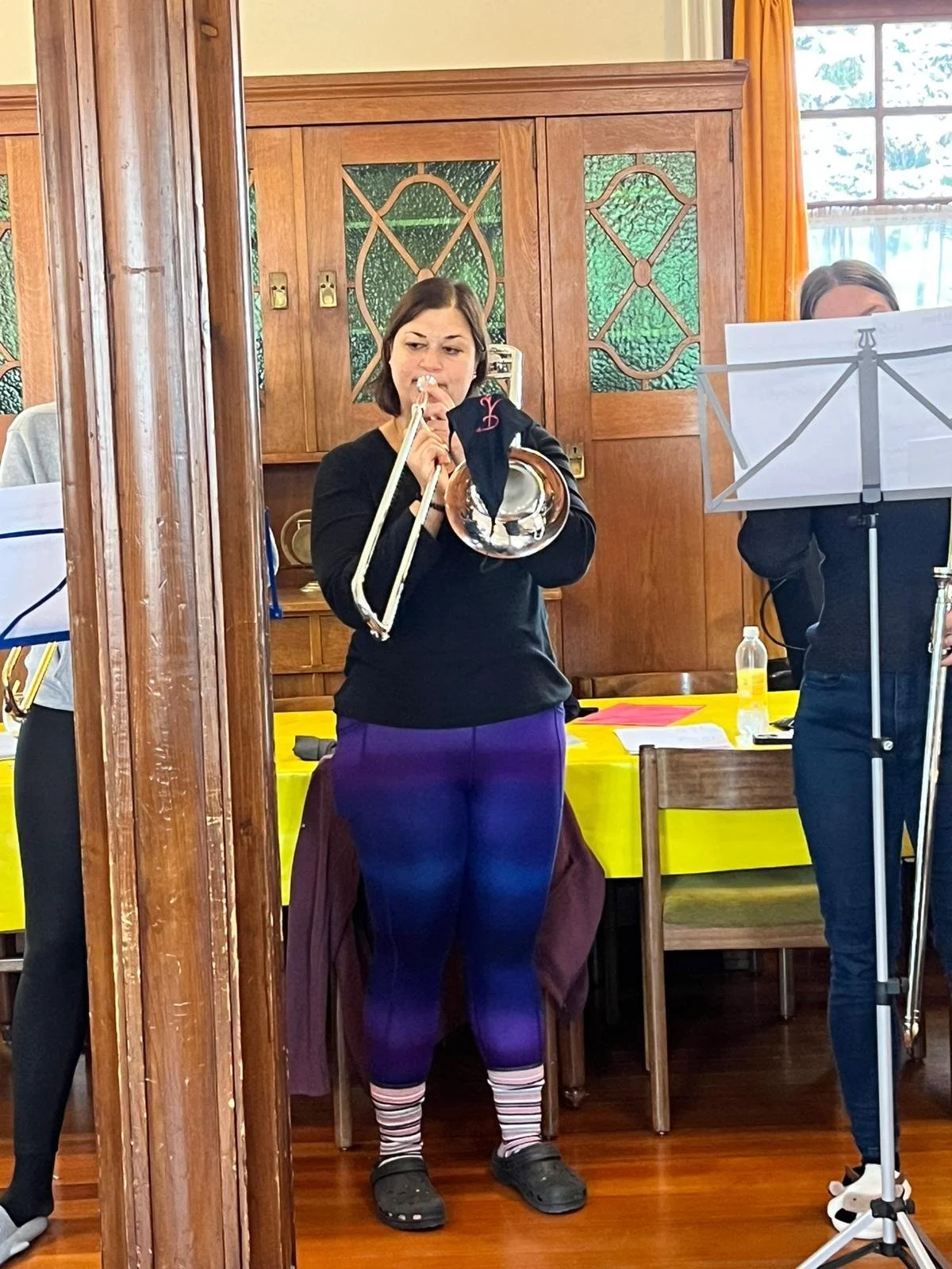 Eine Frau spielt die Trompete in einem Raum mit Holzvertäfelung und gelben Tischdecken.