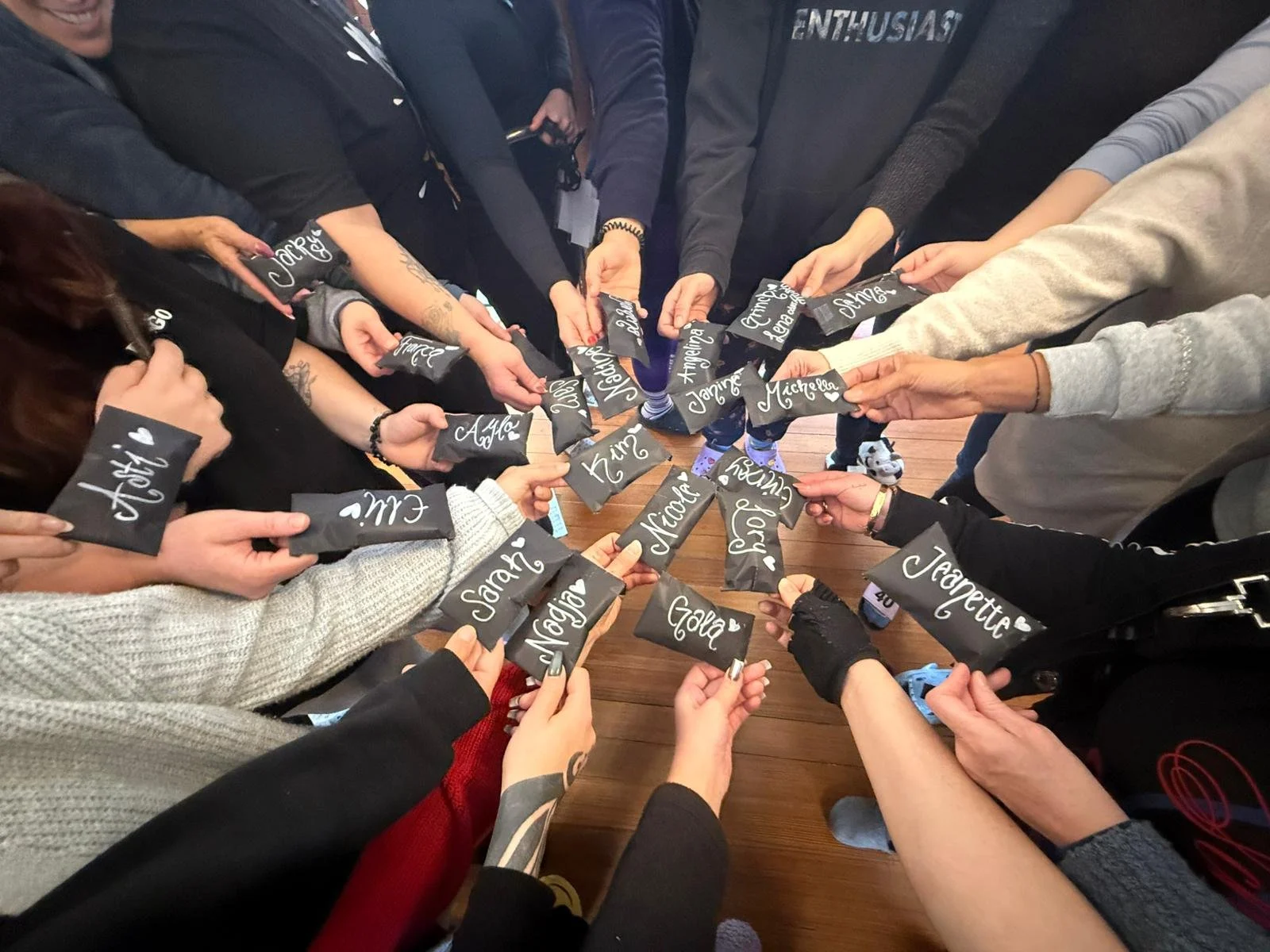 Menschen halten schwarze Geschenktäfelchen mit weißen Namen in einer Kreisformation über einem Holztisch