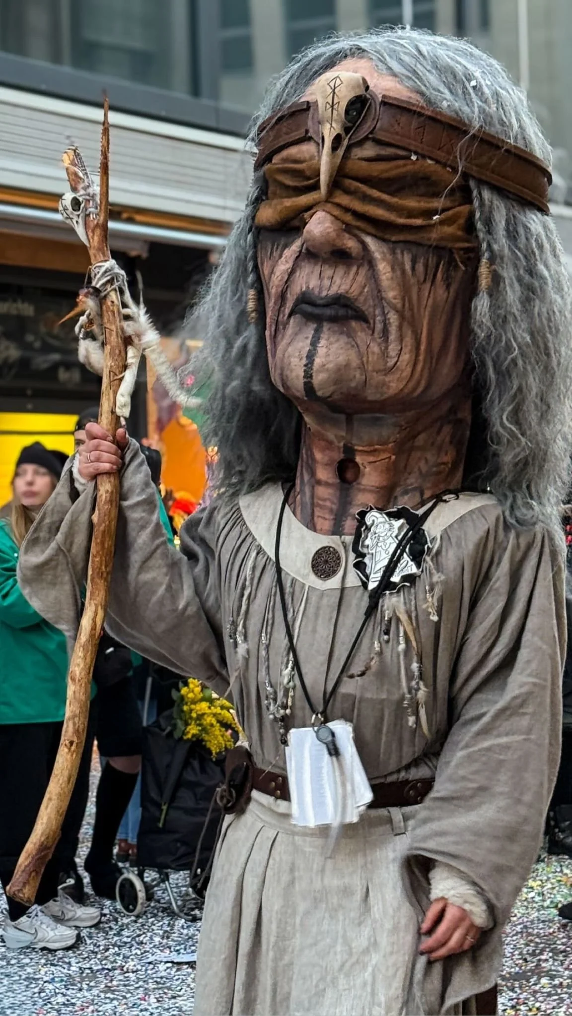 Person in Kostüm eines alten, alten Weisen mit grauem Zottelhaar, einer Augenbinde und einem Stab bei einer Parade oder Fest in einer Stadt.