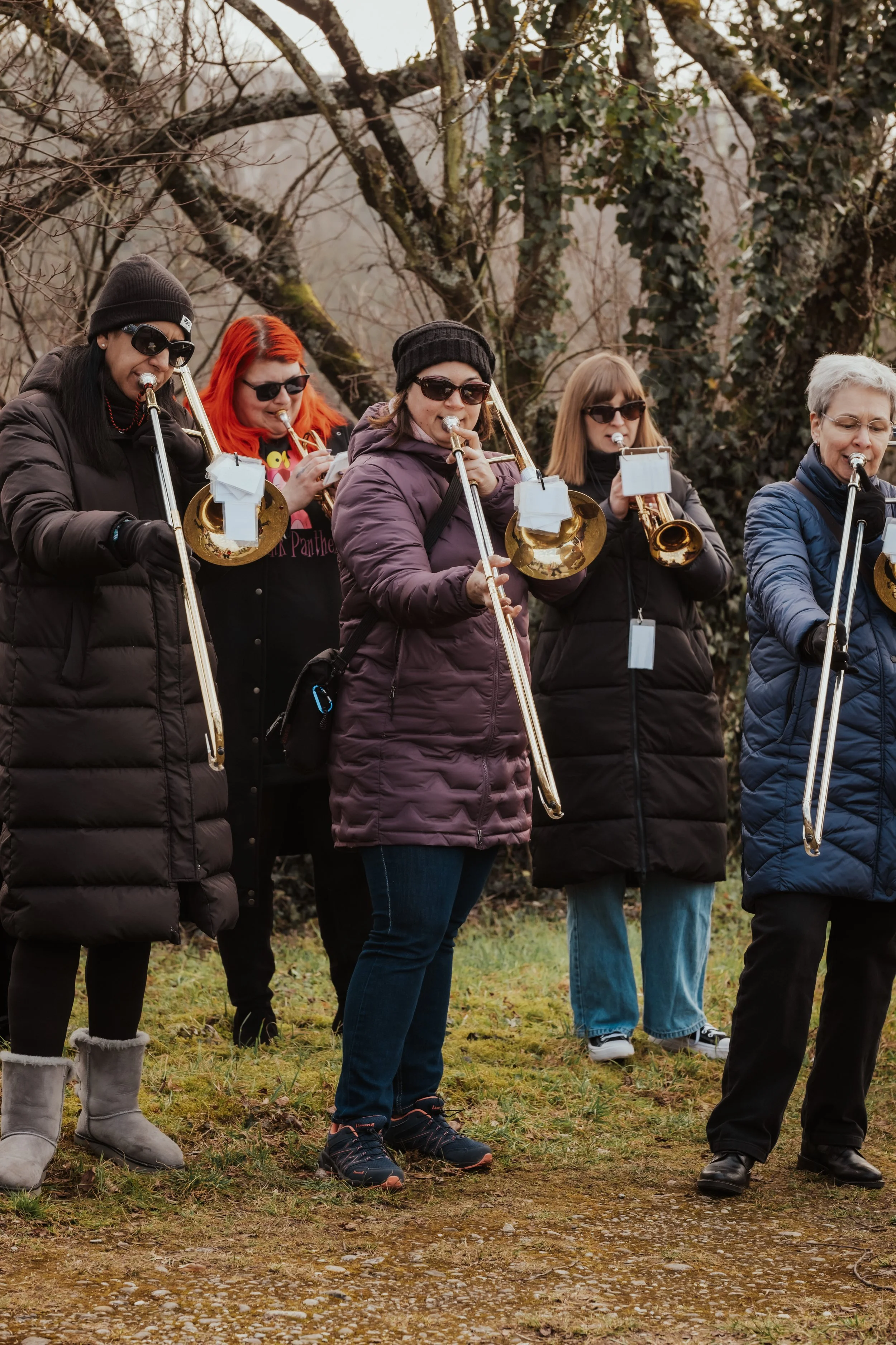 Eine Gruppe von Frauen steht im Freien, alle spielen Trompeten und tragen Winterkleidung