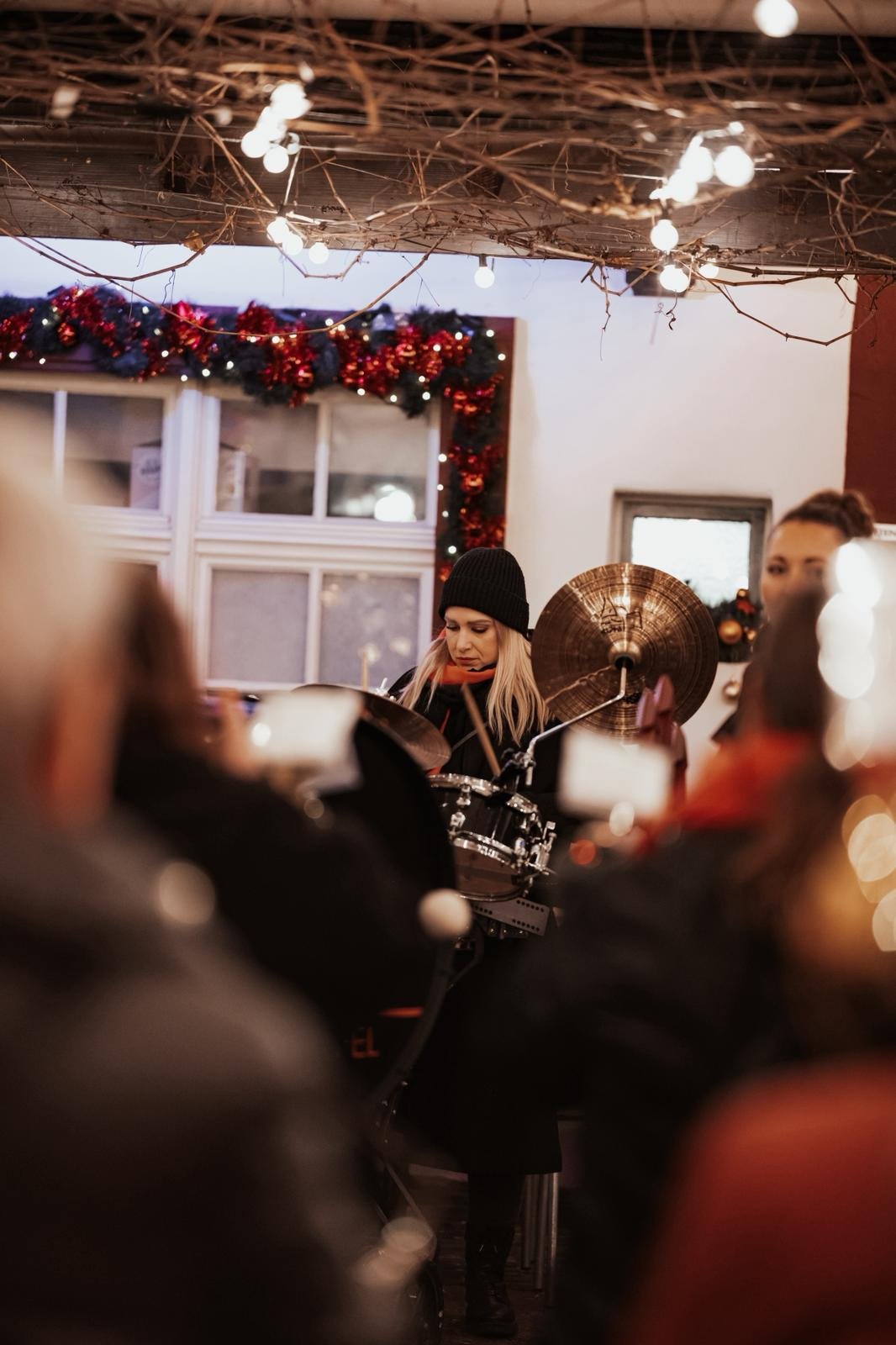 Eine junge Frau spielt Schlagzeug bei einer festlichen Weihnachtsfeier, dekoriert mit Weihnachtsgirlanden und Lichterketten.