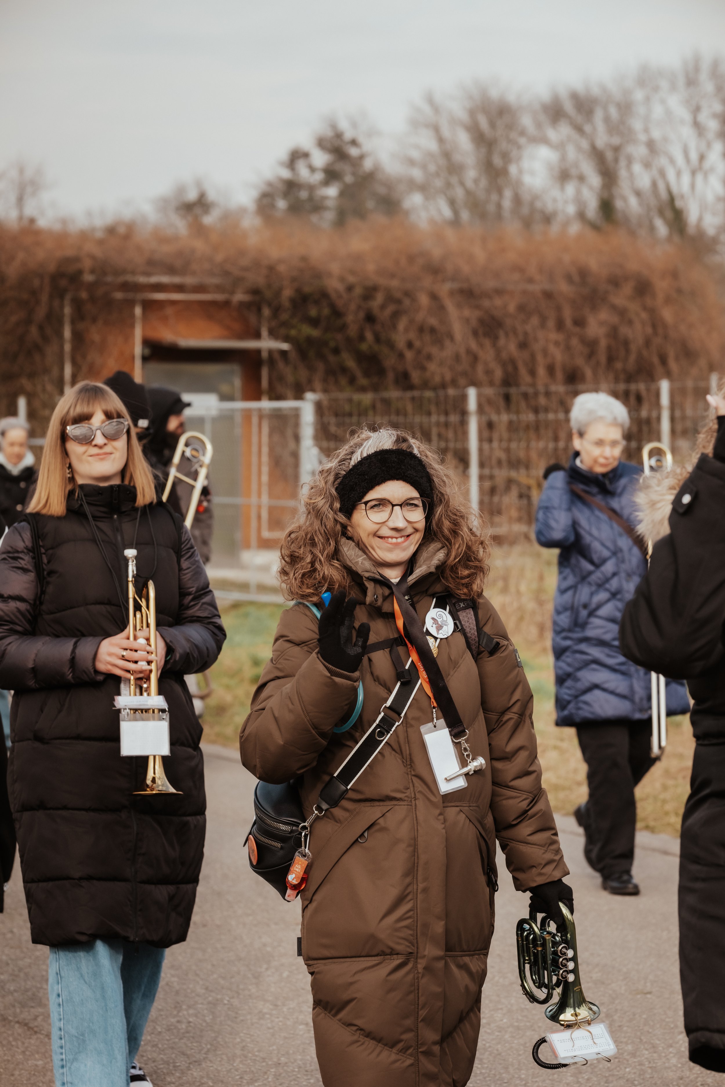 Menschen mit Musikinstrumenten, wahrscheinlich bei einem Musik-Event im Freien, im Hintergrund Bäume und eine Hütte