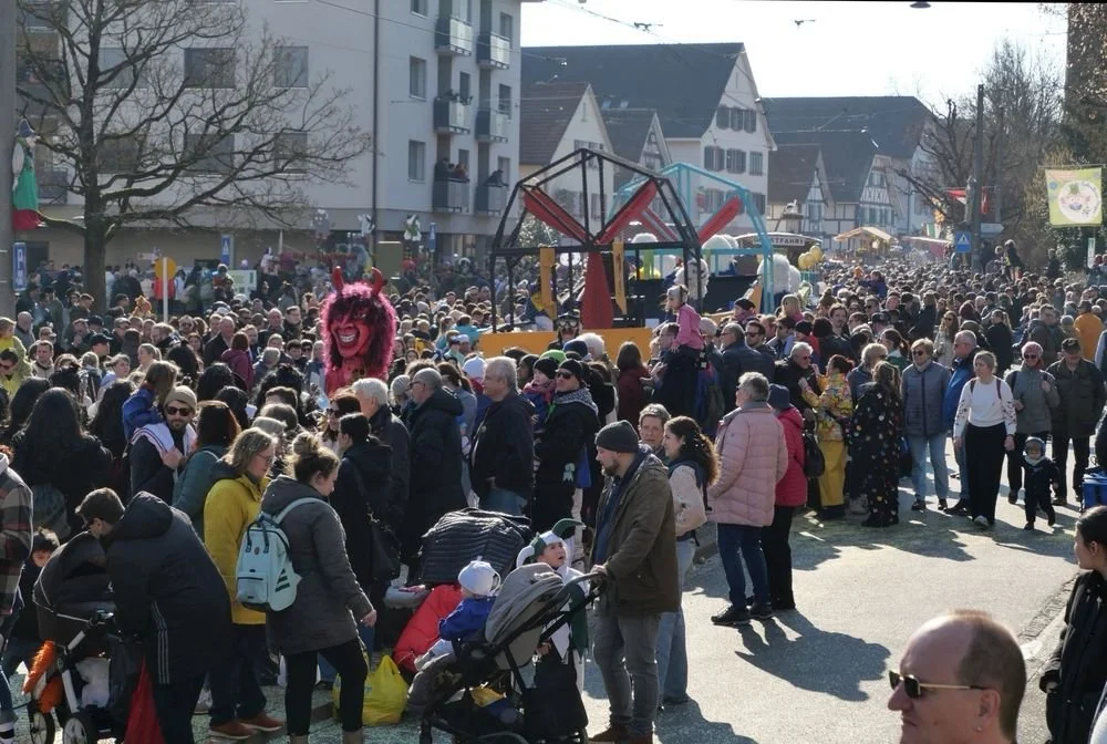 Buntes Volksfest mit vielen Menschen, Karussell, Schaufensterpuppen in Tierkostümen, Hüpfburg, Ständen und Bäumen.