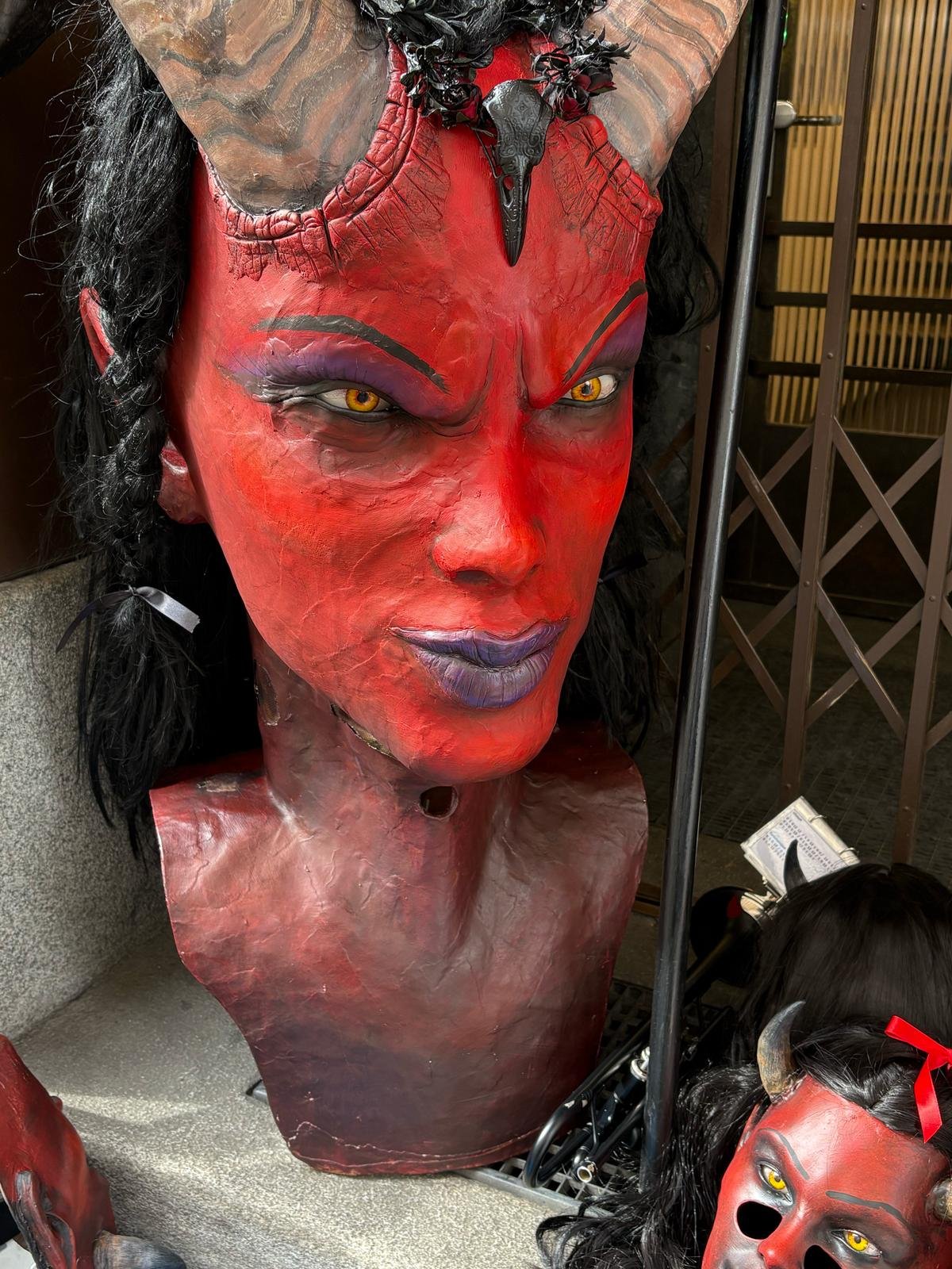 Ein großer, detailreicher Teufelkopf mit roten, schwarzen und lila Farben, Hufen, Hörnern und gelben Augen, auf einem Verkaufsstand.